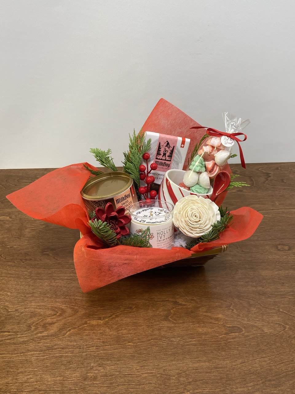 Classic Swiss Holiday Indulgence Basket - Rich, festive, and irresistibly cozy, the Classic Swiss Holiday Indulgence Basket is a luxurious treat for the senses. Featuring premium Swiss chocolate, a hand-poured seasonal candle, soft holiday meringue, and a festive mug, all nestled among fresh winter greenery and red accents. This basket is perfect for creating a warm fireside moment during the holidays. For the delux version we add a beautiful holiday greeting card.  Perfect for: Chocolate lovers, couples, and elevated holiday gifting.