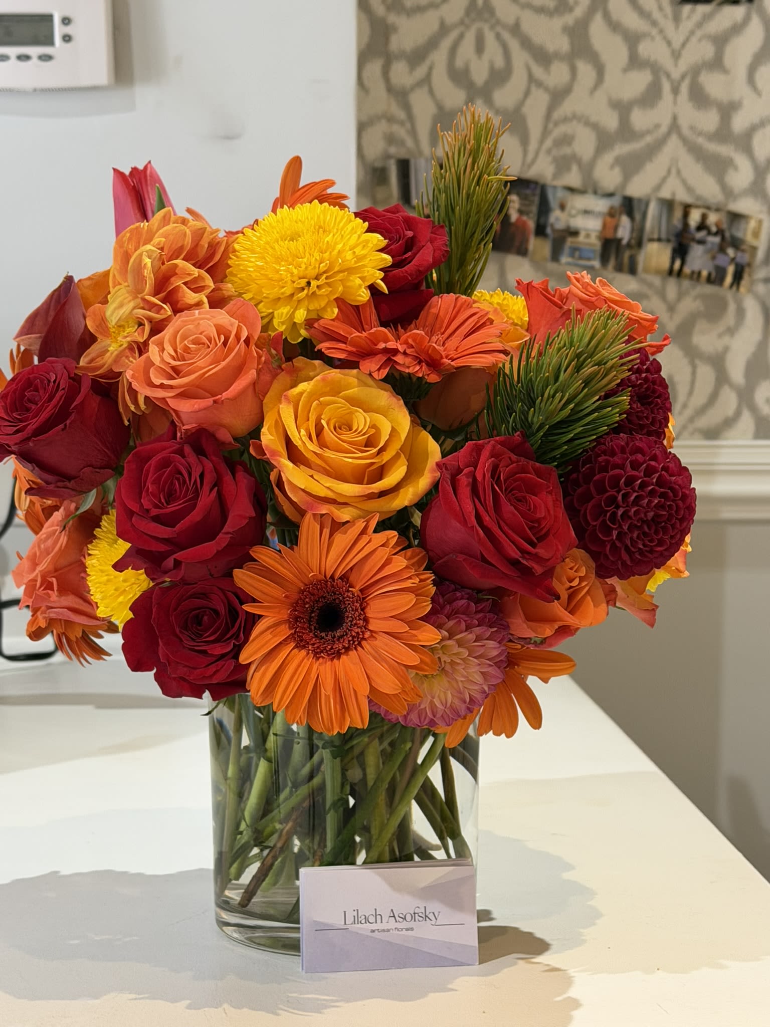 Autumn Gems - Oranges, golds, and reds at their best! An arrangement so happy you can almost see the flowers smiling. Various types of dahlias, roses, gerberas, and foliage work together to create a lasting spell. - Available year-round.