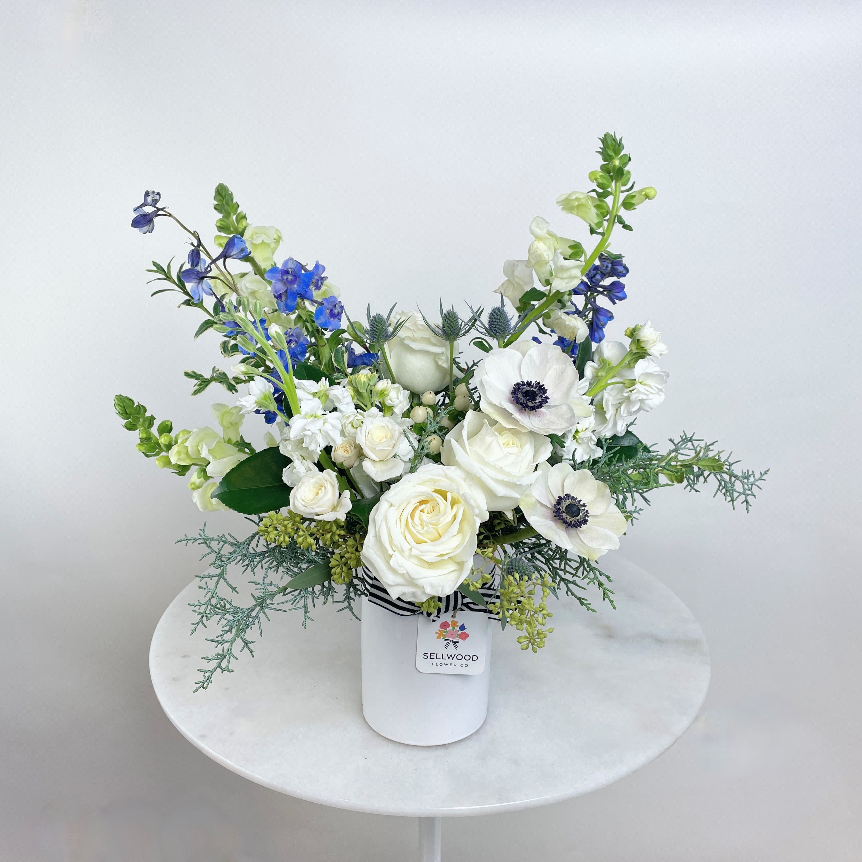 The Winter Blue Ice - Elegant and refreshing, this arrangement features lovely white blooms, vibrant blue delphiniums, and delicate anemones, accented with soft greenery. A stunning choice for a sophisticated display!