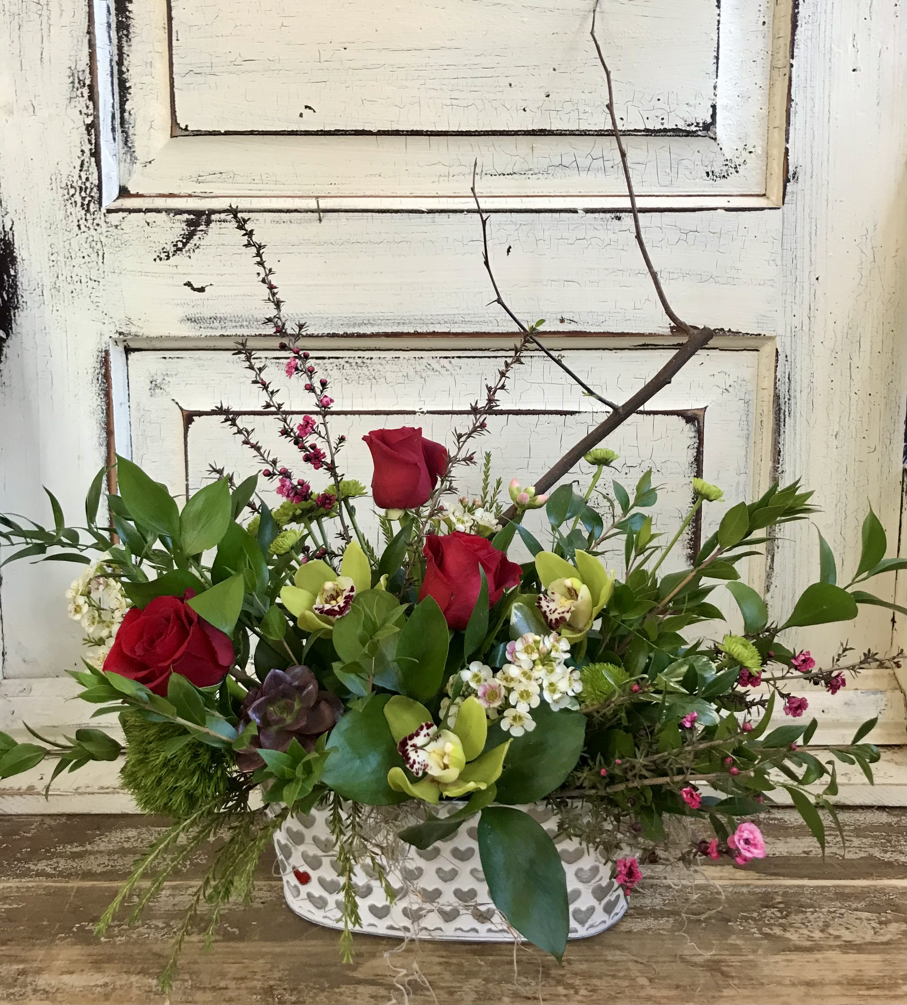 I "Heart" You - An oblong metal container embossed with mini hearts is designed for the table with a collection of unique textures and blooms including orchids, red roses, a mini succulent and branches.
