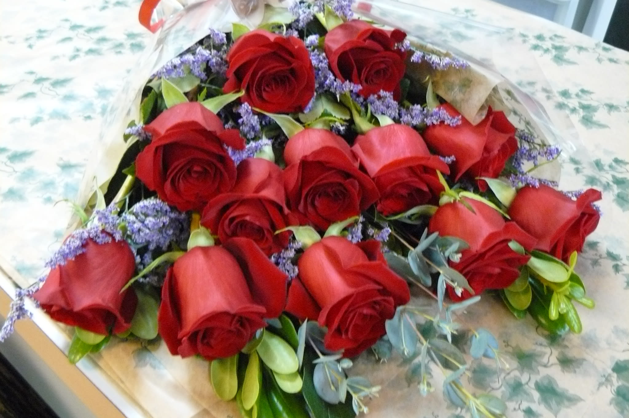 Traditional  1 Dz. Long Stem Red Roses Wrapped -  1 DZ.  Freedom Long Stem Red Roses,  Fancy Assorted Greens. Call for Color Rose Preference. 