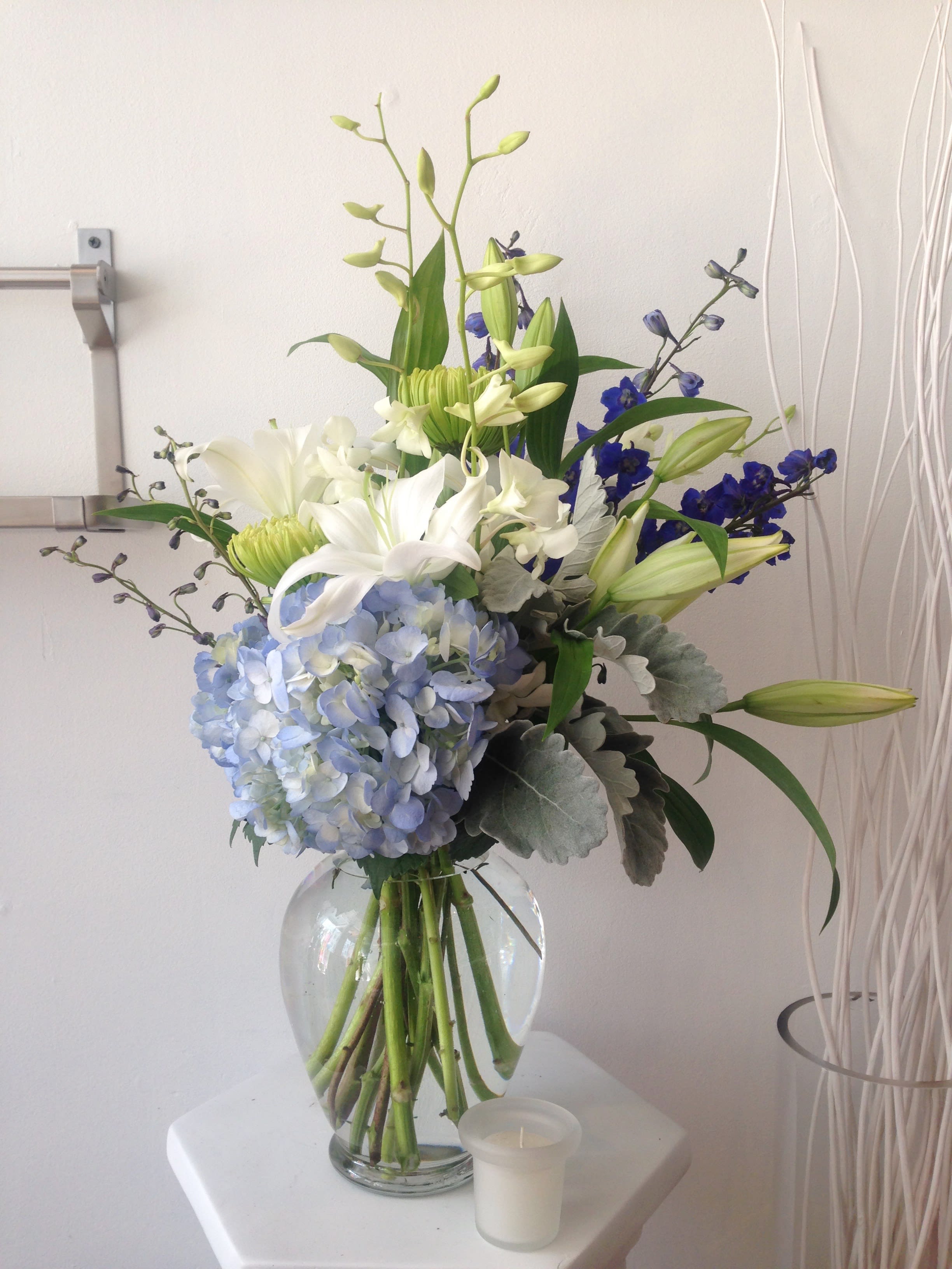 Ocean Blue. A Floral Archist™ Design. - Delphiniums, Bells of Ireland, *Lilies, Hydrangeas*, Iris, Orchids, and other seasonal blooms. It is a great gift for a birthday, get well, sympathy expressions, wishes for a fresh start. PJf reminds you that guys love flowers too!    Male appropriate or anyone who just loves blue.   *Shade of blue varies. *Lilies are poisonous to CATS.  NOTE: Our flowers and greens are a gift from nature. It’s shade and depth might vary, design, value and aesthetic remains the same. In support of our efforts to aide in the preservation of our planet, PJf uses Fair Trade flowers, Plants, Upcycled and Recycled containers. 