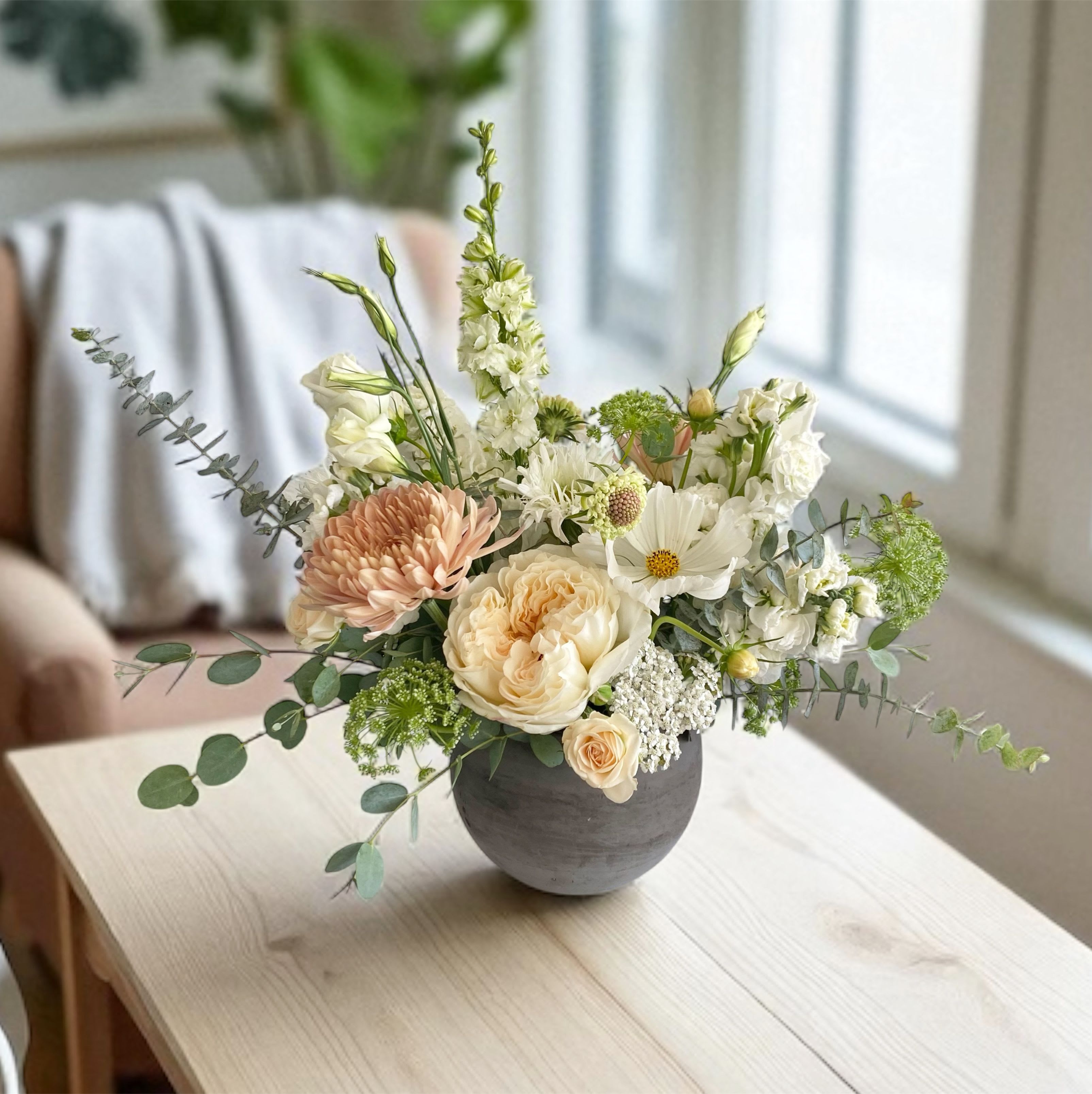 Boho chic - Bring effortless elegance into your home with our Boho Chic Arrangement. Designed in a sleek, charcoal or gray vase, this hand-crafted bouquet blends soft, romantic blooms in shades of cream, blush, and peach, as  it captures the natural beauty of an English garden with a modern twist.  Perfect for brightening up a living space, gifting for special occasions, or adding a touch of refinement to any room, this arrangement exudes calm sophistication and timeless charm.  Details:     •    Comes arranged in a reusable ceramic vase     •    Fresh, hand-selected seasonal blooms     •    Ideal for home décor, gifts, or intimate events  For same day delivery please call 949-682-5004. Vase, flowers and colors are based on availability. 
