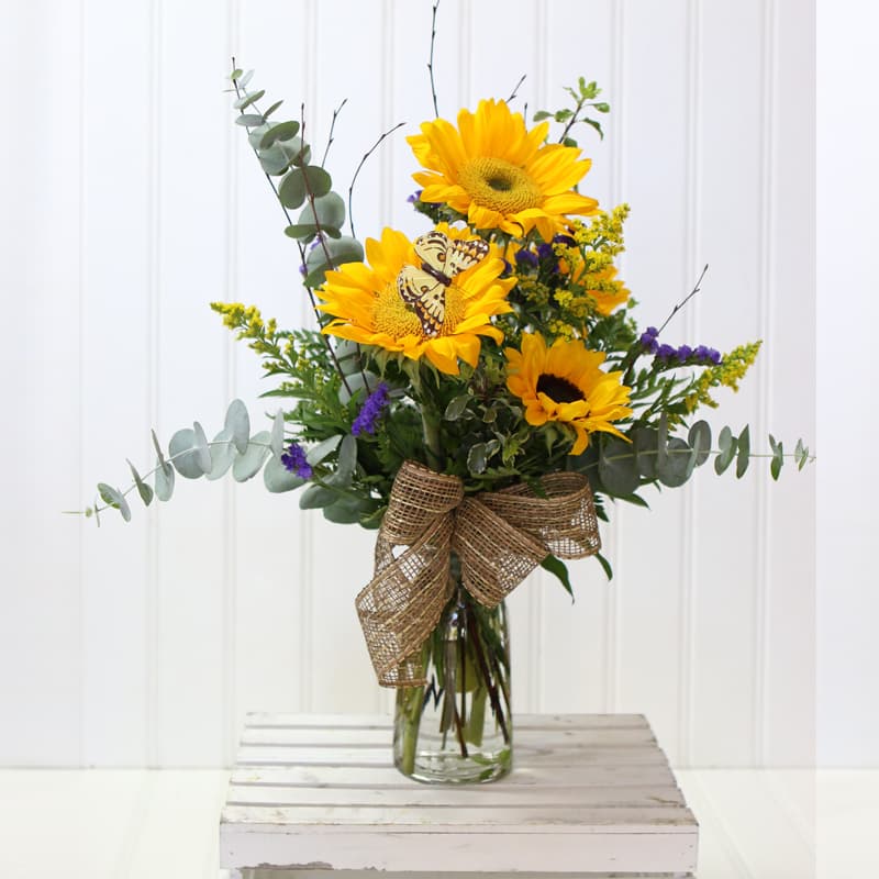 Papa Smiles - Sunny sunflowers mixed greens purple status birch branch and solidago in a clear vase .This would brighten anyone’s day and put a smile on their face.    