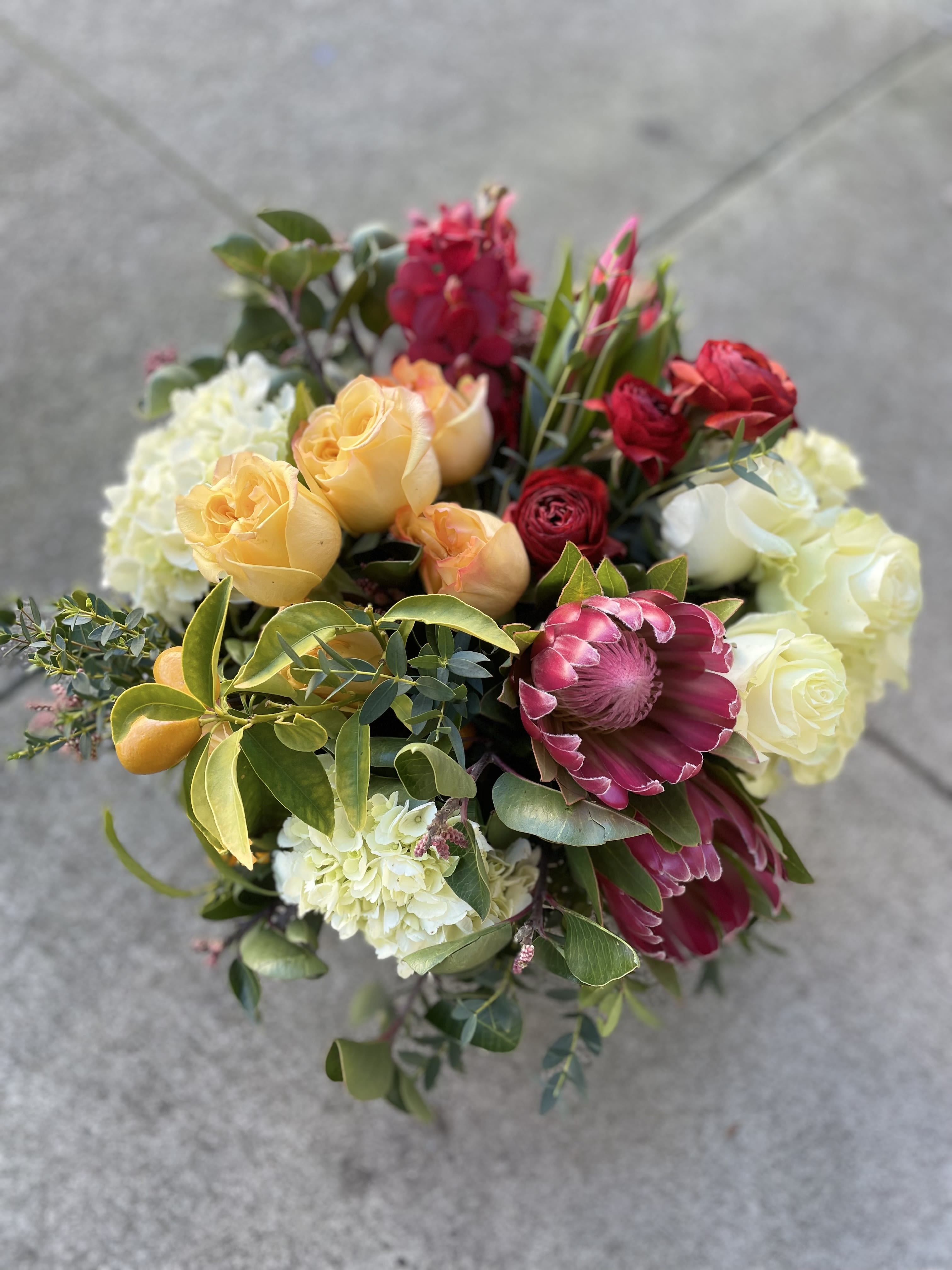 Lunar Love  - Designers Choice in rosy red, whites, and golden orange/peach with a pop of kumquats on the vine for good luck! Seasonal substations may be made if a flower or element is not available.   