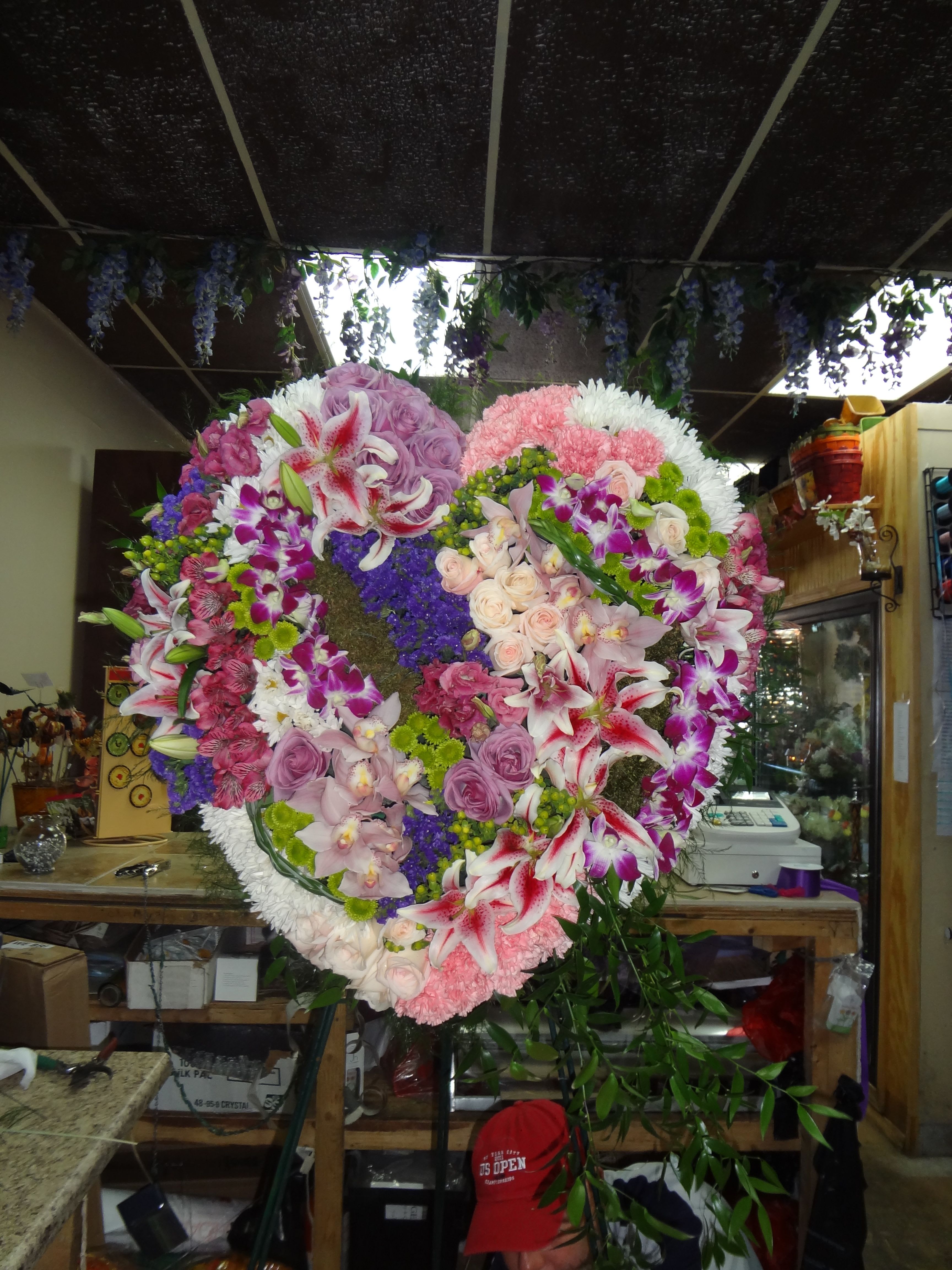 Forever in our hearts - mix soft heart colors, delicate with ,roses,orchids Lilly,carnations,green buttons  Make a strong, stylish statement of love with this beautiful heart-shaped . Presented on a funeral easel, the rich  rose sympathy arrangement is a lovely standing spray to place on the altar or by the entrance to the service. Presented on a traditional wire easel for ease of placement.. Orientation: One-Sided  SUBSTITUTION POLICY – Always deliver the freshest flowers! Please note the bouquet pictured reflects our original design.  If the exact flowers or container in this arrangement are not available, our local florists will create a beautiful bouquet with the freshest available flowers.