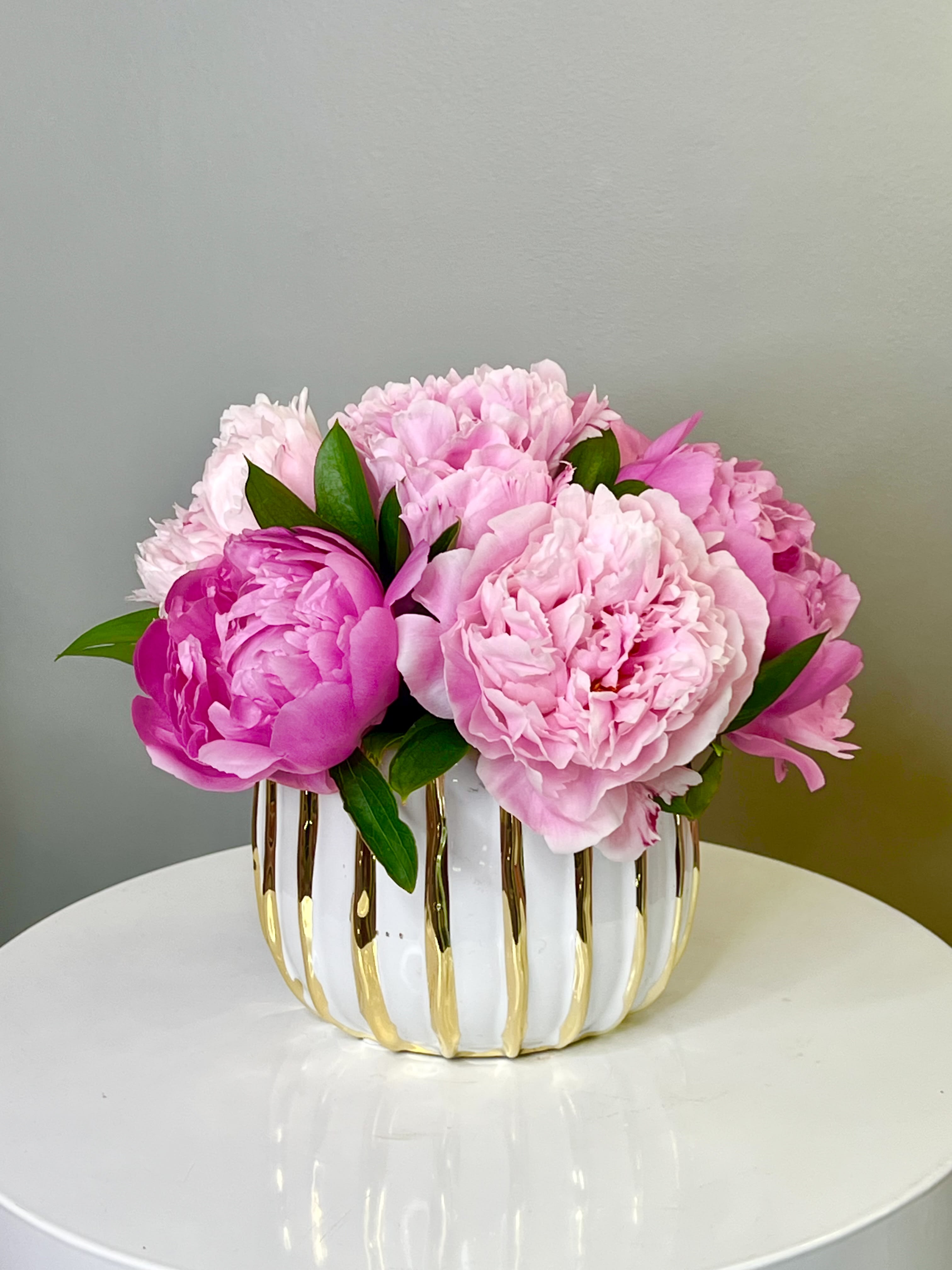 Peonies Dream ™ - A luxurious display of rare seasonal peonies in shades of blush and magenta, arranged in a white-and-gold striped vase. Their lush petals make this piece irresistibly elegant and romantic.