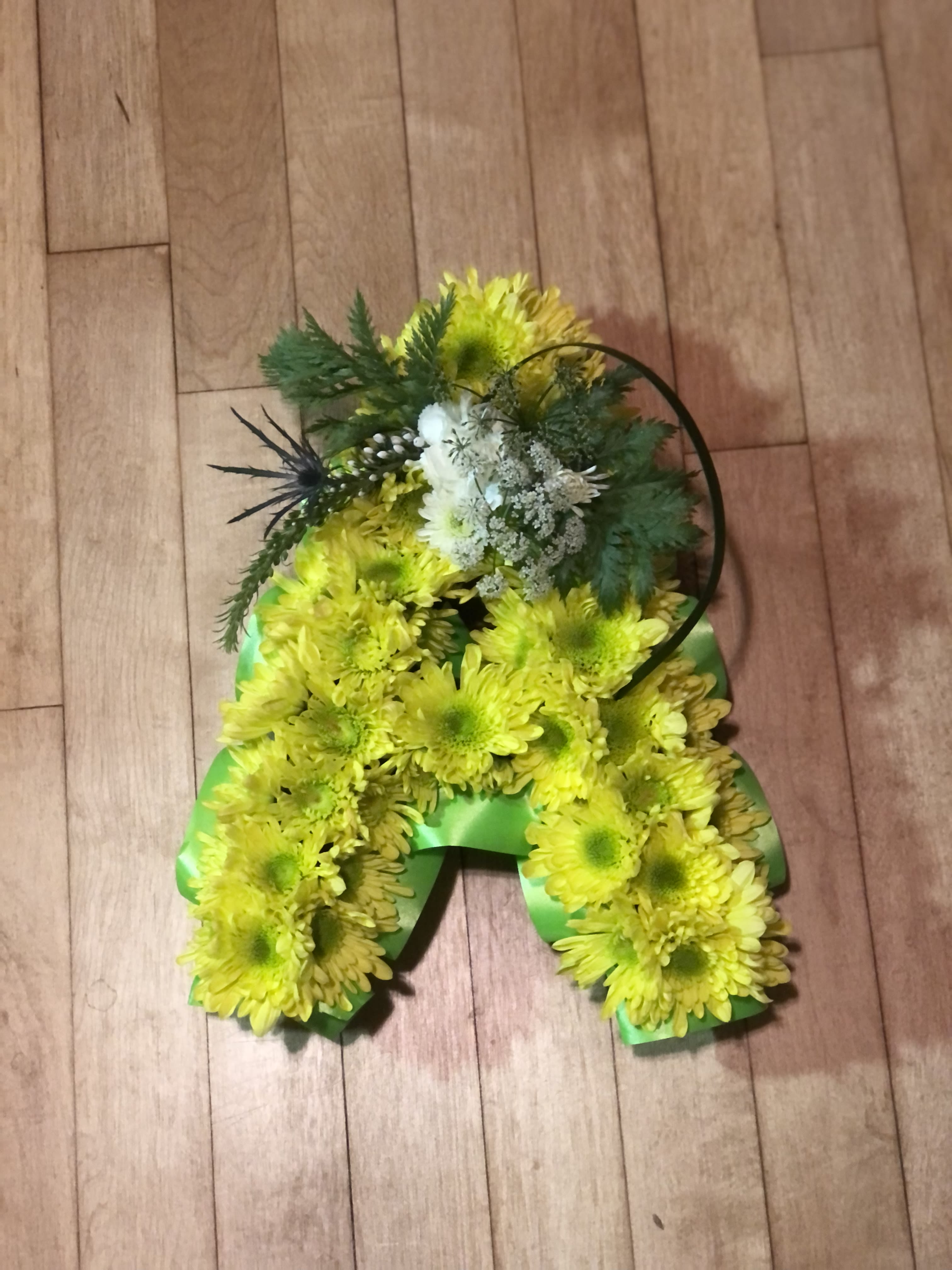 Tribute letter - 11 1/2" tall letter covered in chrysanthemums with a floral focal point front and center. Trimmed in waterproof ribbon. Many letters available. (special order needs 3 1/2 weeks lead time.) Spelled names will be an additional price. ( up to 4 letters are possible) Displayed flat.