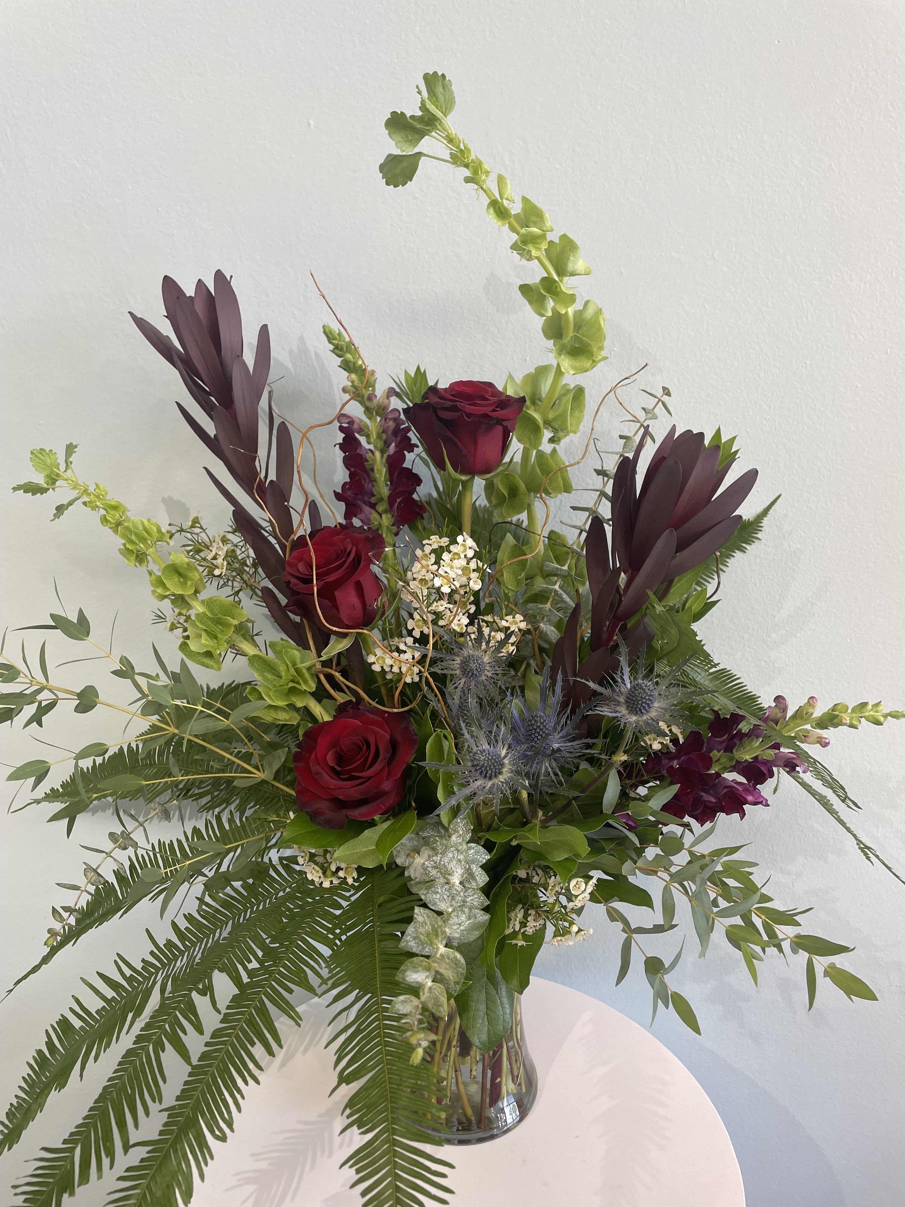 Woodland Dream - This moody, woodsy arrangement is perfect for any occasion! This arrangement exudes fall vibes and may consist of dark red roses, leucadendron, snap dragons, blue thistle, and an assortment of stunning greens such as eucalyptus and waxflower.