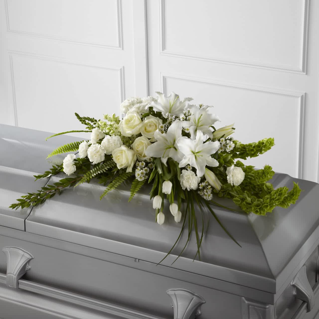 Resurrection Casket Spray - The Resurrection Casket Spray inspires thoughts of comfort and peace to those wishing to pay their respects for the loss of the deceased. White tulips, roses, snapdragons, Oriental lilies, larkspur, carnations and Monte Casino asters are accented by the bright green stems of Bells of Ireland and an assortment of the finest lush greens to create the perfect arrangement to display on the top of their casket during their final farewell service. Approximately 40"W x 24"D.