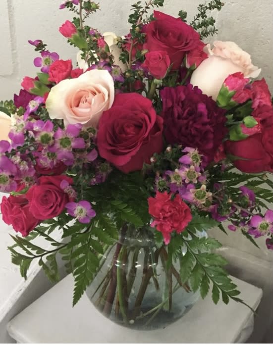 Blooming Love - Hot pink roses, light pink roses , purple wax,hot pink spray roses,plum carnations nestled in a low vase with greens 