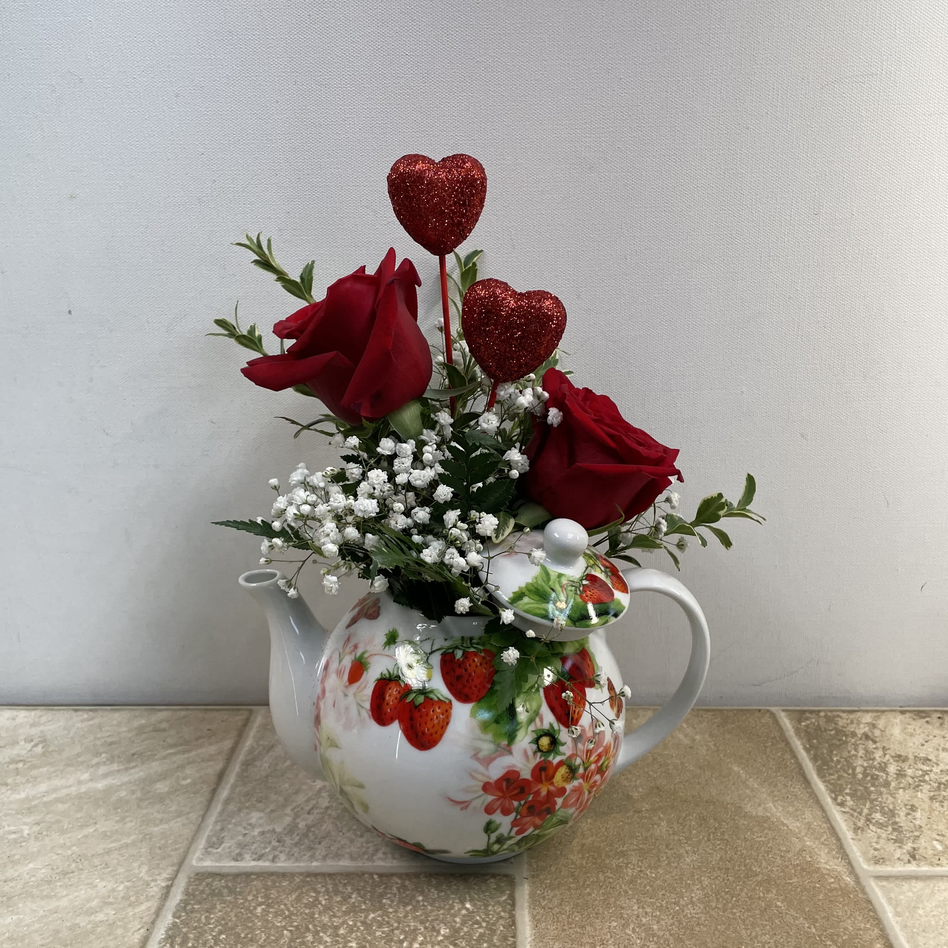 Tea for Two - Tea for Two is meant for you and your sweetheart. Two red roses, glittered hearts and baby’s breath are perfectly arranged in a lovely ceramic teapot decorated with a medley of strawberries and delicate blooms. Approximate size: 10” wide x 12” tall.  Primary flowers: rose