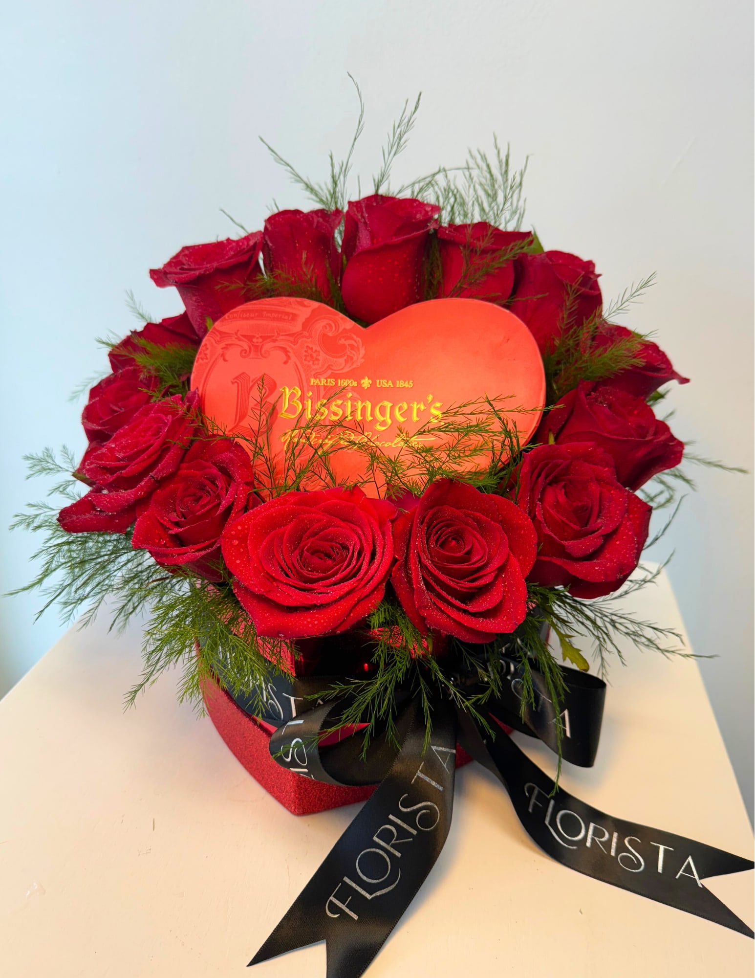 COCO TEMPTATION - A dozen velvety red roses beautifully arranged in a heart-shaped box, embodying timeless romance. Centered with a heart-shaped box of gourmet chocolates, it’s the perfect gift to express love and indulgence.