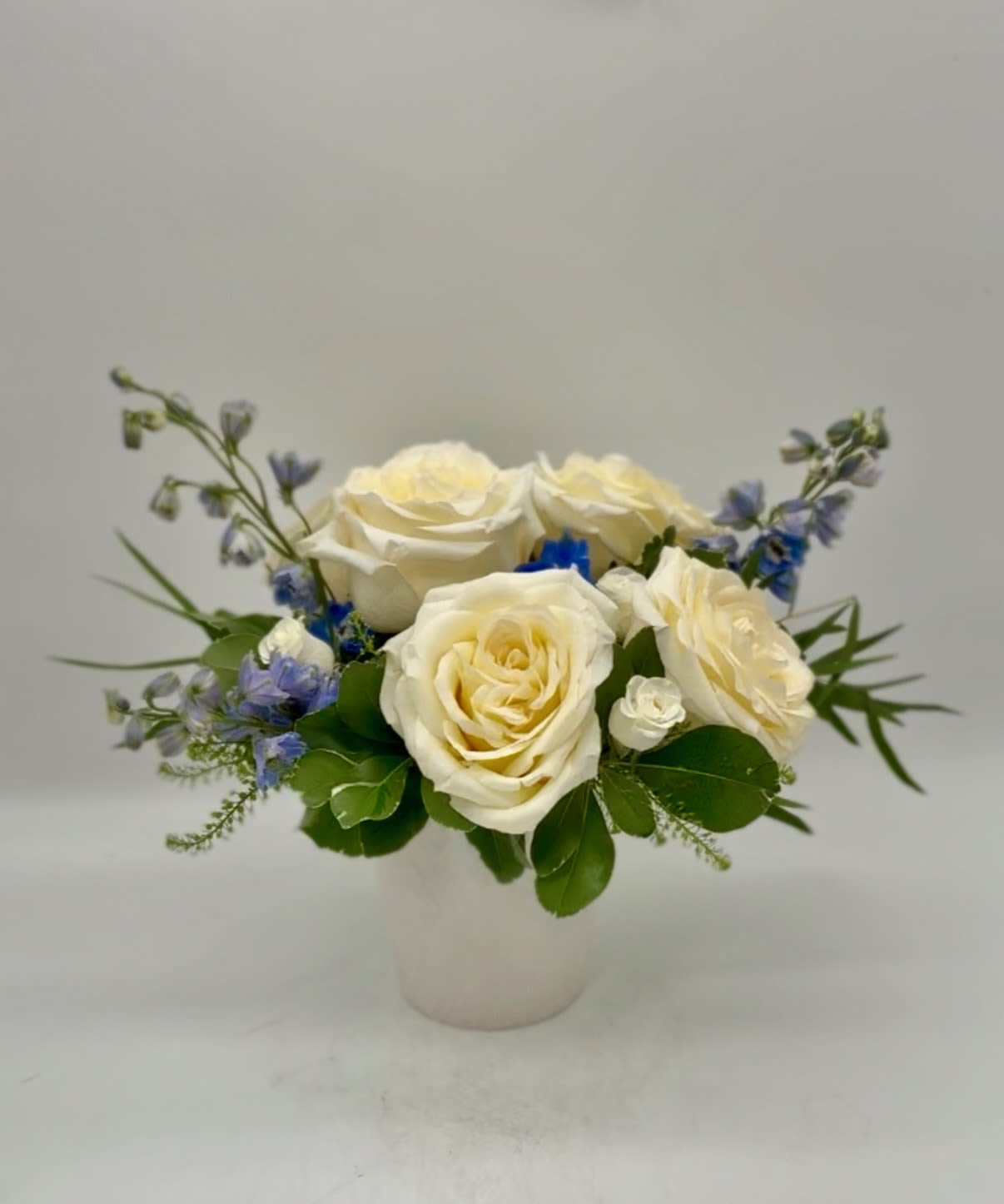 Candlelit Tides - This modern display highlights 'Candlelight' garden roses (our owner's favorite variety), accented by blue delphinium and white spray roses. The natural pastels are reminiscent of the Atlantic coast beach scenes and relaxing times in the sun. Perfect for anniversaries, congratulations, just because, or to put on your own table! Two sizes to choose from.