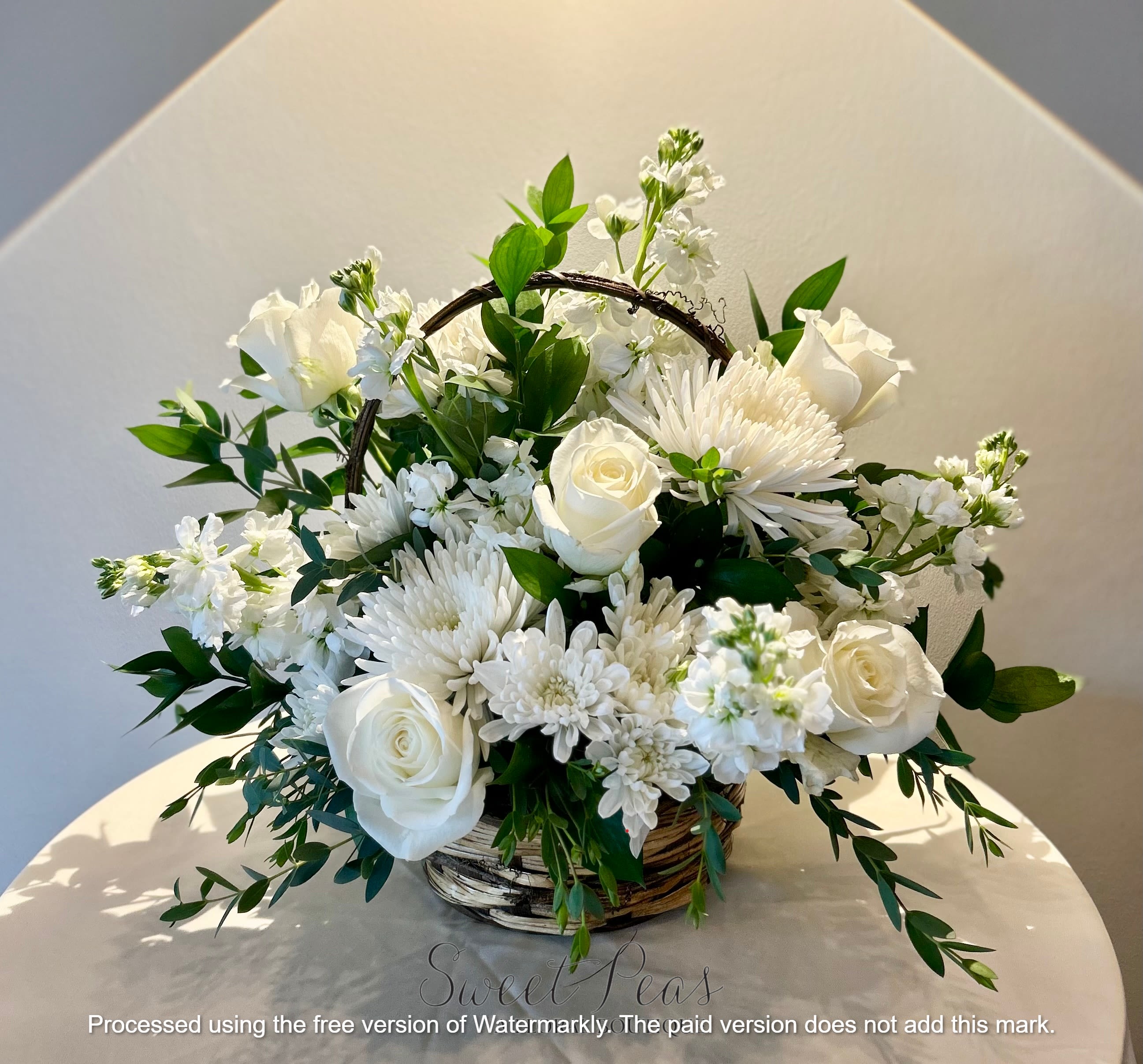 Eternal Grace - This arrangement is so serene and classic—pure white roses, mums, stock, and lisianthus, softened with lush greenery and designed in a rustic wicker basket. It feels timeless, peaceful, and comforting, perfect for both elegant occasions and thoughtful sympathy pieces.