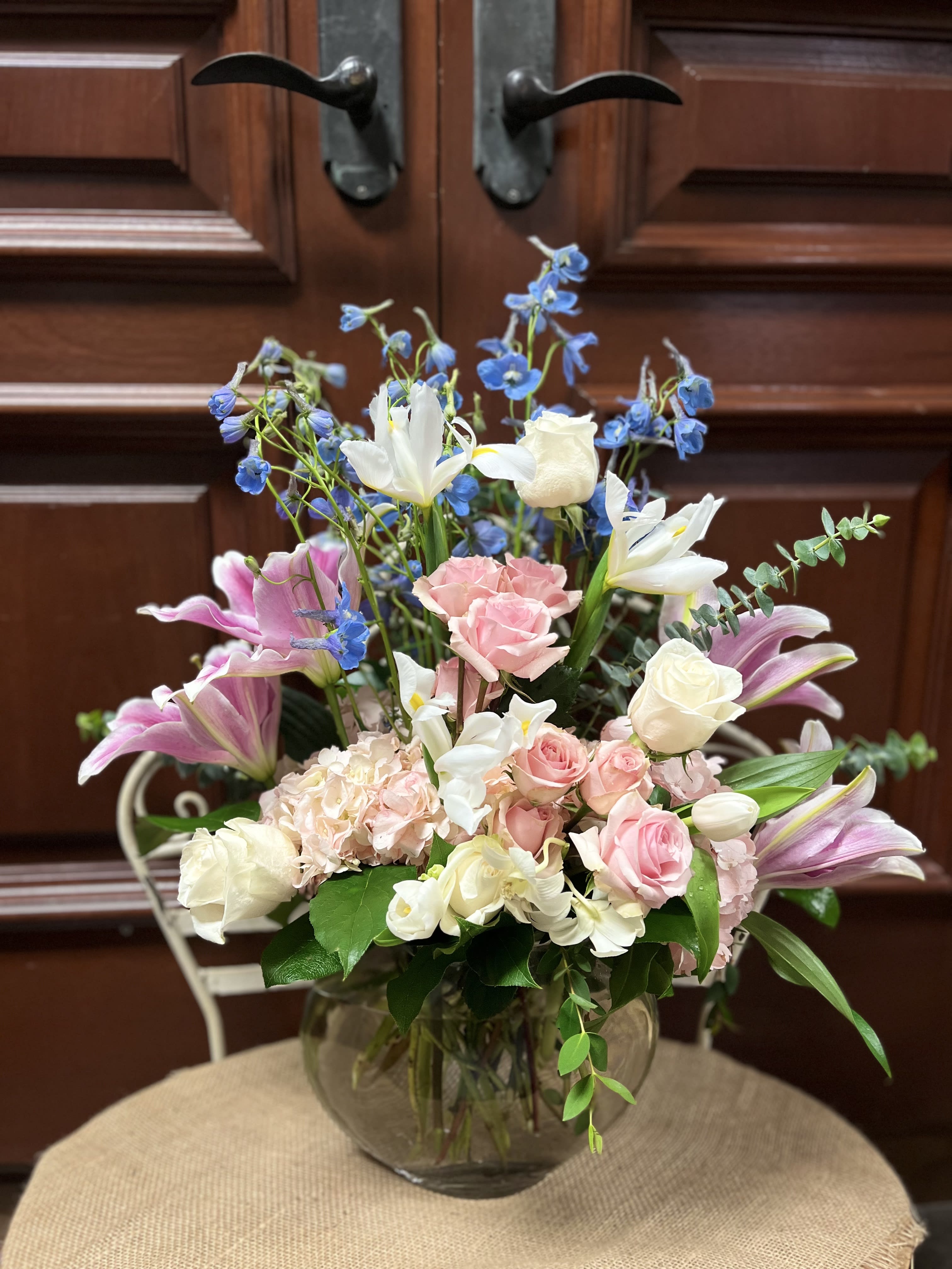 iridescent blooms - Recipe: Blue Delphinium, White Iris, Pink Spray, White Tulips, Pink Stargazers and eucalyptus in a white, oval clear vase. Availability: All year round Design View: Symmetric Front Facing View Photo shown: Standard 