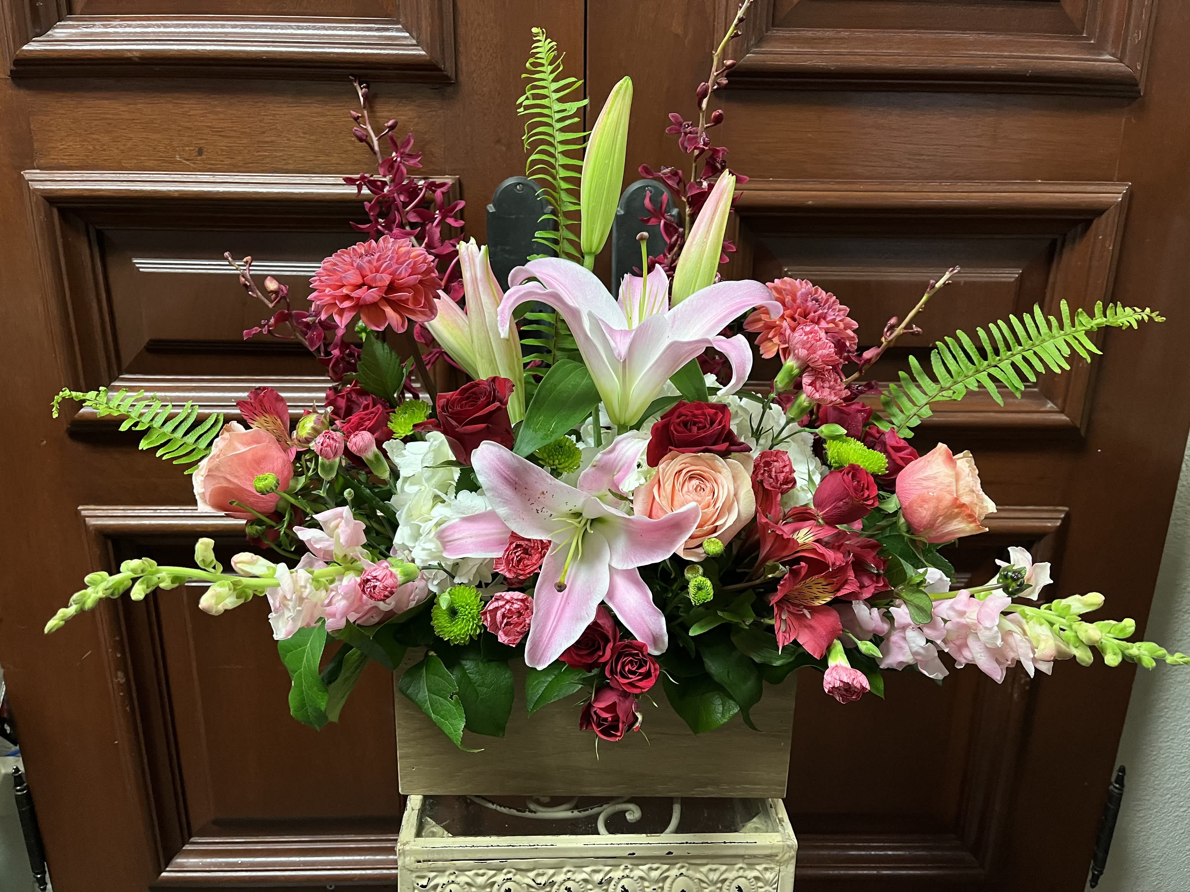 More Than A Woman - Recipe: Seasonal Dahlias, Burgendy Orchids, Stargazers, Orange/Pink Roses, Pink Snapdragons, Red Spray Roses, Red Alstromerias, Pink Carnations, Green Buttons, and more in a local, hand-made wood box. Season: Seasonal Dahlias Design View: Symmetric Front Facing View Photo shown: Standard 