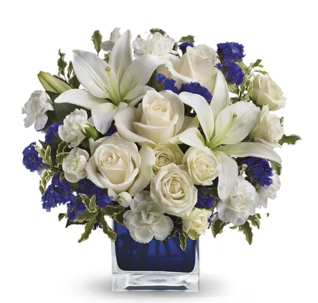 Forever Blue Cube - Nothing better to inspire a bouquet than nature itself! Our Clear Blue Skies Bouquet is arranged to reflect the beauty of a beautiful day where the sun is shining without a cloud in the sky! Pearly white lilies surrounded by creme white roses purple statice invoke happiness in any beholder, whether they're displayed in a home or at an office, they're perfect for any kind of day.  Includes: • Creme Roses • Creme Spray Roses • White Asiatic Lilies • White Miniature Carnations • Purple Statice • Blue Cube Vase
