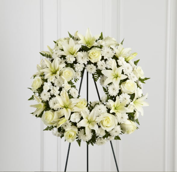 Treasured Tribute Wreath - The FTD Treasured Tribute Wreath offers peaceful wishes of heartfelt sympathy with each delicate bloom. Bright white roses, Asiatic lilies, mini carnations and cushion poms are beautifully arranged to form an elegant wreath accented with lush and vibrant greens. Displayed on a wire easel, this gorgeous tribute is a wonderful symbol of eternal life and sweet serenity.