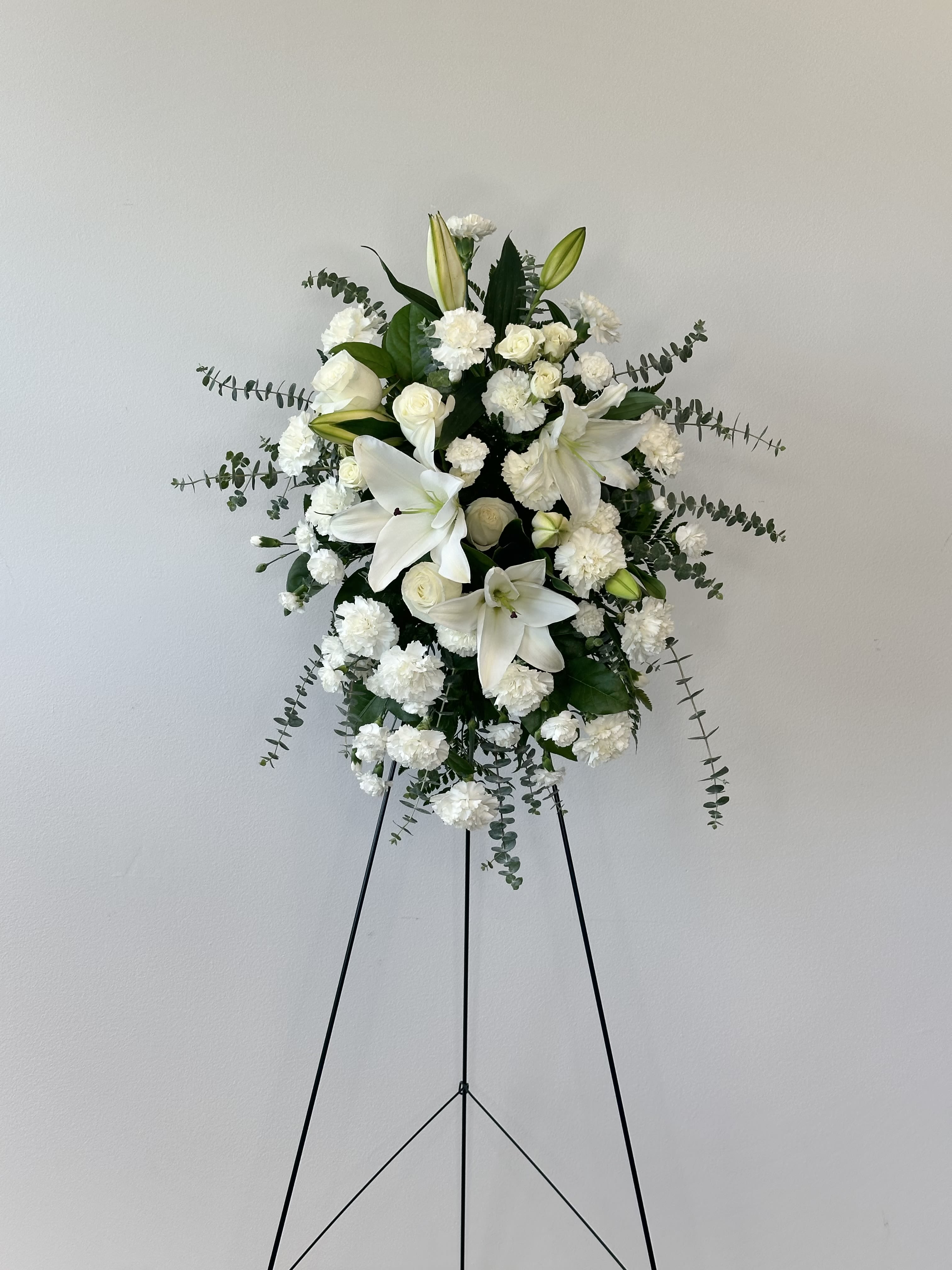 Serenity Spray - A gentle touch for tender moments. The Sentiments of Serenity Spray from Irvine Village Flowers offers a quiet, comforting embrace through flowers, perfect for sharing sympathy with care. This simple yet lovely arrangement features white roses, white Asiatic lilies, and white carnations, tied softly with a white satin ribbon and framed by gentle greenery. Standing at about 25" W x 35 1/2" H, this one-sided spray is a thoughtful way to show you’re there when words feel too heavy.  Each bloom speaks softly: white roses carry peace and respect, their calm beauty a steady presence in tough times. White Asiatic lilies bring a sense of purity and quiet hope, their graceful petals offering solace. White carnations add a layer of remembrance and tender love, lasting long to honor what’s been lost. Together, with assorted greenery, they create a serene tribute that feels like a warm hand on the shoulder—a small gesture with big meaning.  Visit Irvine Village Flowers online or in-store to send this gentle spray, delivered fresh and ready to bring a bit of peace to those who need it most. We’re here to help you share your heart, simply and sincerely.