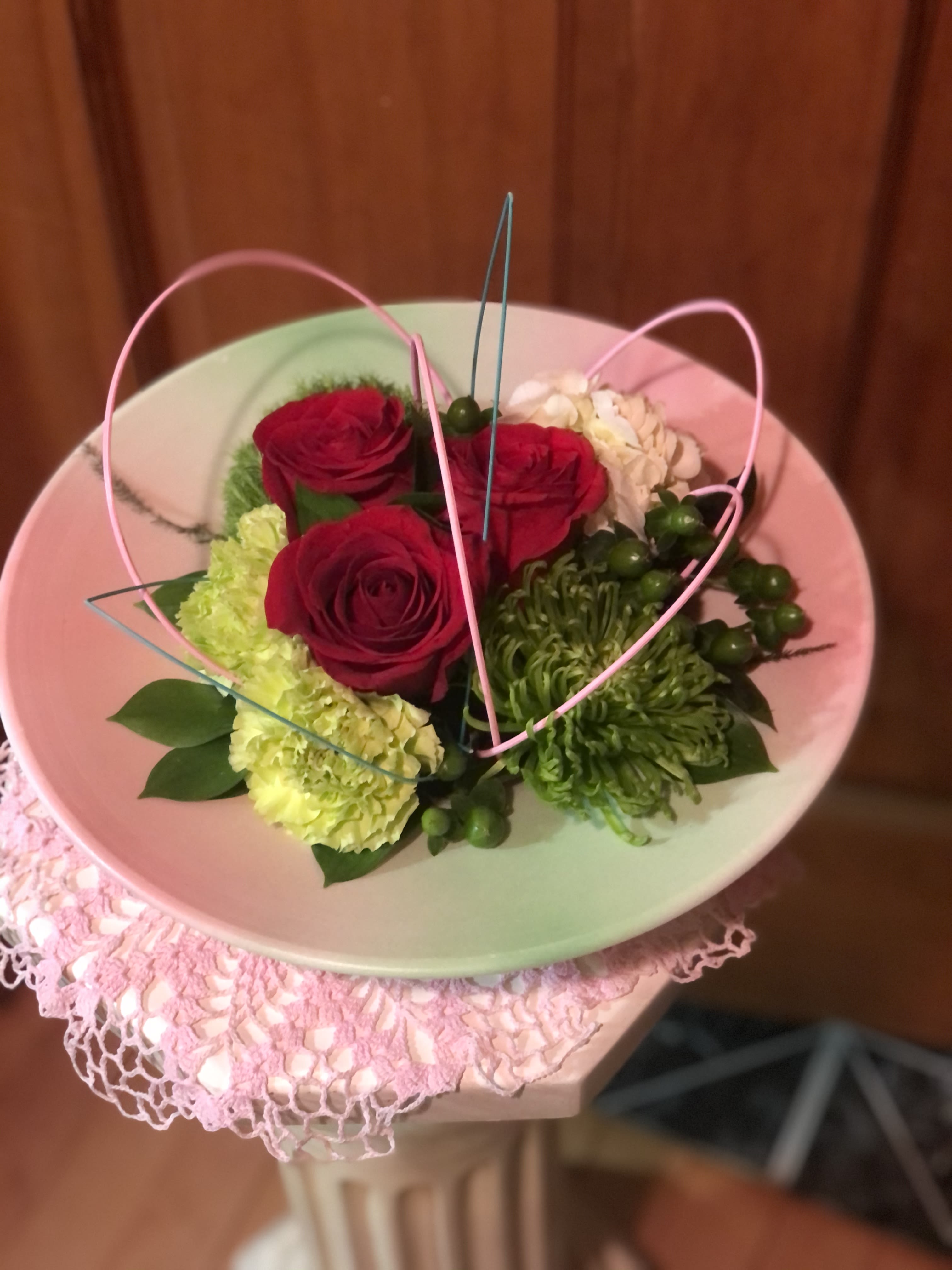 Encircled with Love - Encircled my Love begins with a round softly colored tray. Built with 3 Premium Red Roses, 1 Hydrangea, 1 Green Trick, a few Carnations and a single Fiji Mum. Accented with Hypericum Berries and assorted greenery. Off-set with arched Midollino sticks for effect. Sure to stir feelings in whomever receives this wonderful design.