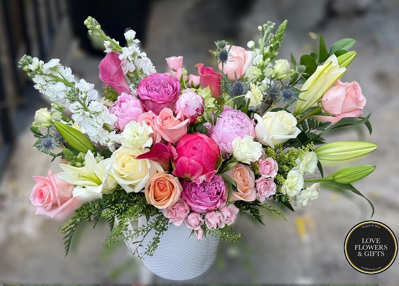 Mixed arrangement of pink peonies, roses, and lilies in a white ceramic vase