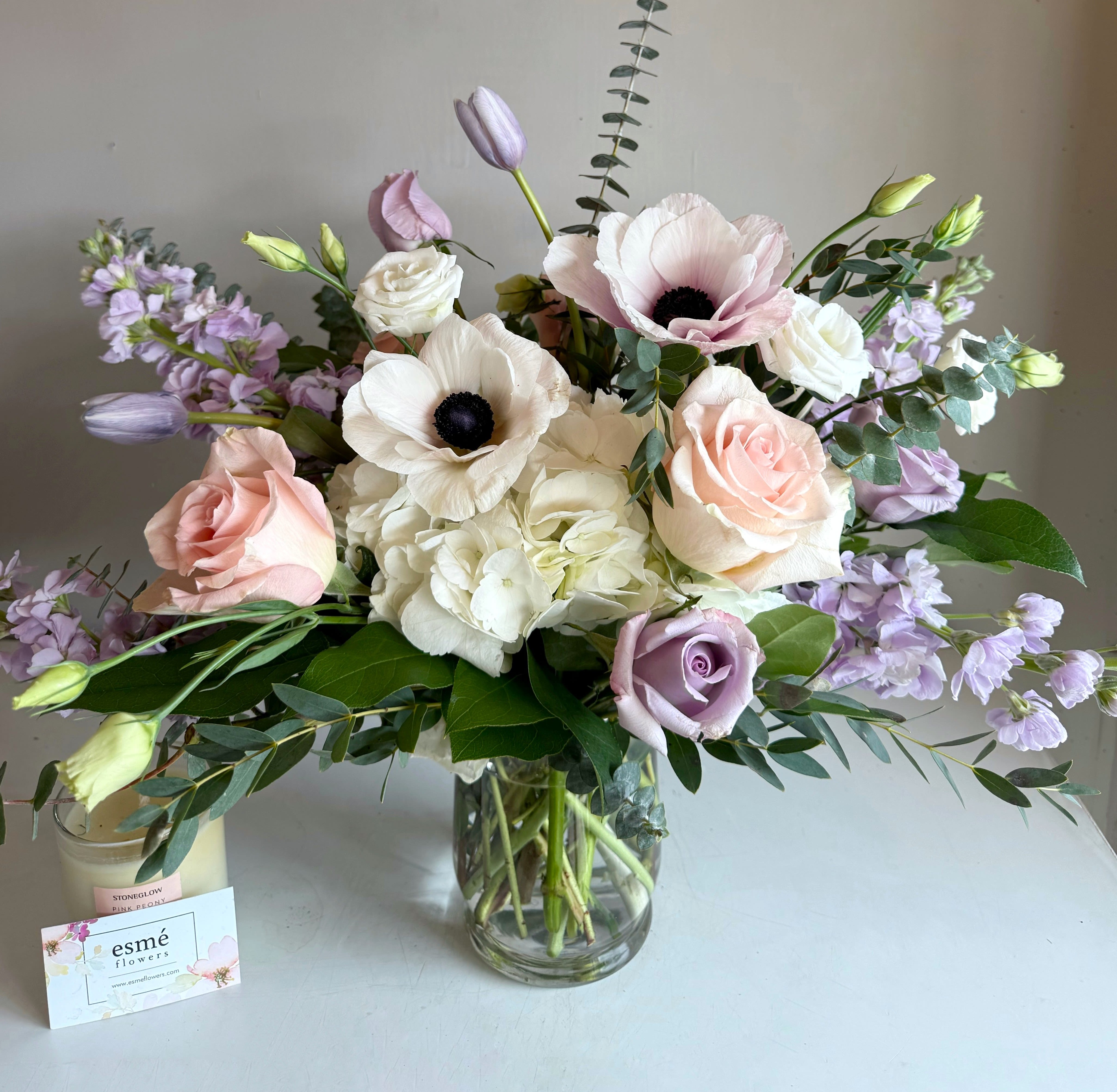 Anya - A delicate harmony of white, lavender, soft pink, and blush blooms, arranged to evoke a light, soft and airy energy. Flowers featured include Italian Mistral Anemones, ocean song roses, lisianthus, stock, hydrangeas, and blooms in season.