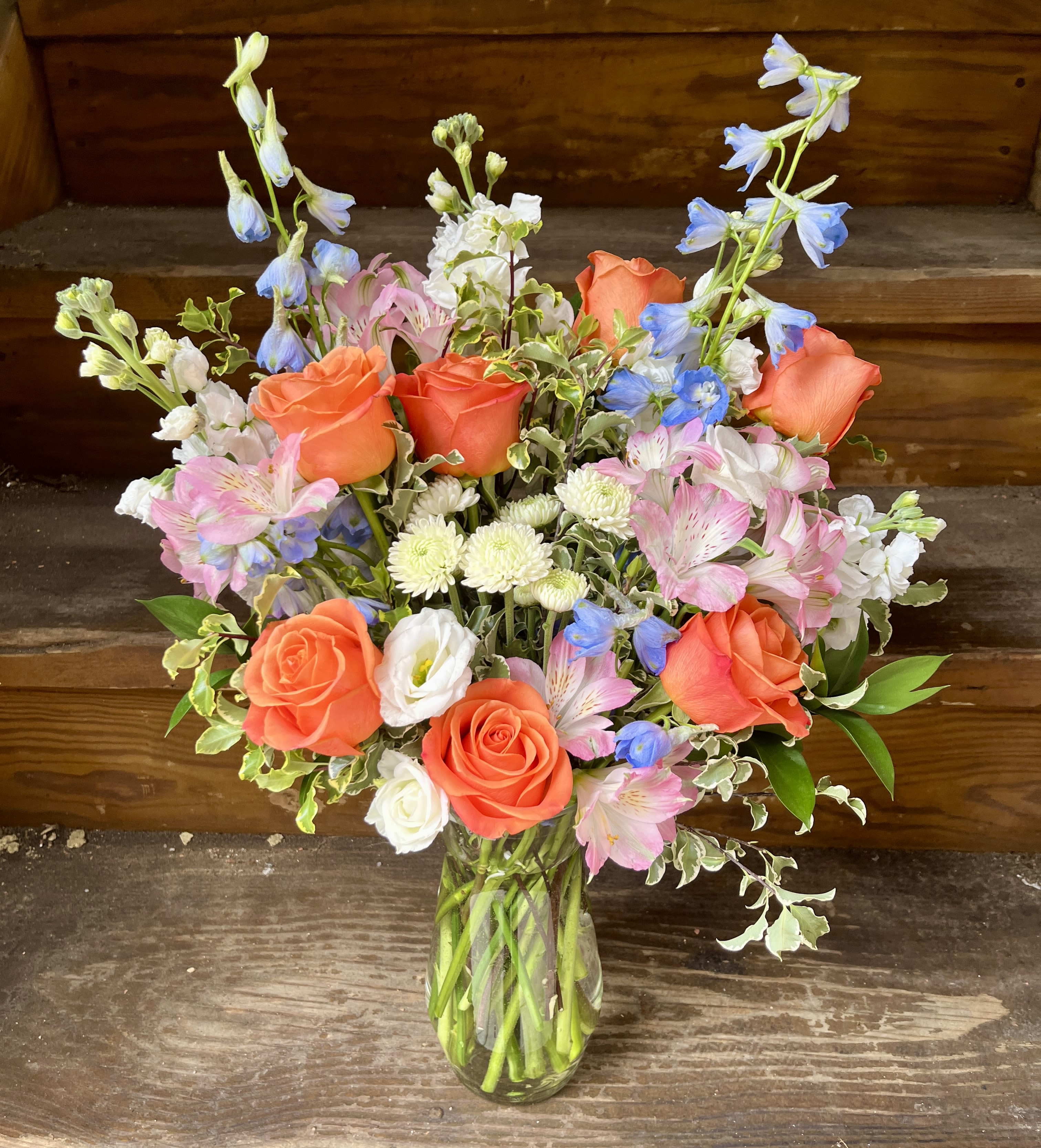 Yesterday’s Sunset - A tall elegant design of blue delphinium, light pink alstromeria, fragrant white stock, orange roses and accent florals and soft flowing greens. 