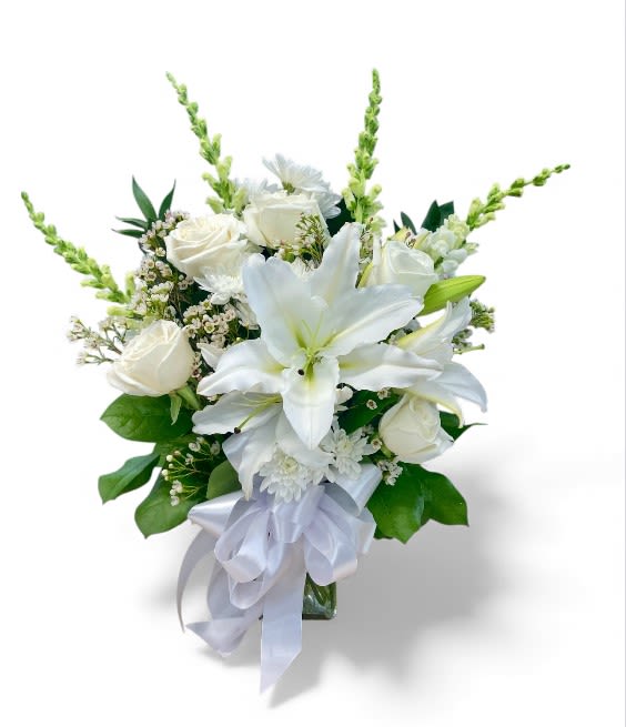 Eternal Memories Vase - This elegant sympathy arrangement is beautifully showcased in a 7" rectangular vase, conveying a sense of serenity and grace. Adorned with lush foliage, this bouquet features four exquisite white snapdragons that symbolize strength and resilience. Six pristine white roses express love and respect, while the Asiatic lily adds a touch of purity and remembrance. Complementing this harmonious arrangement are two delicate stems of white waxflower, representing enduring love and beauty. Together, these blossoms create a heartfelt tribute, offering comfort and solace to those in mourning.