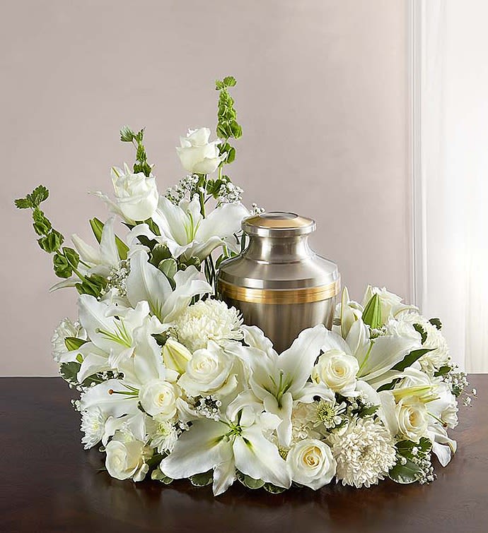 Cremation Wreath - All White - Honor a life so beautifully lived. Our florists artistically hand-design an asymmetrical all-white table wreath arrangement with roses, lilies, carnations and more. An urn or framed photograph can be placed in the open center, creating a comforting tribute for the cremation or memorial service. Our florists hand-design each arrangement, so colors and varieties may vary due to local availability Asymmetrical arrangement of white roses, Oriental lilies, football mums, carnations, cushion poms, gypsophila, Bells of Ireland and variegated pittosporum Send to the cremation service or memorial service; urn or framed photograph can be placed in the center Large arrangement measures approximately 18"H x 18"L Small arrangement measures approximately 17"H x 14"L