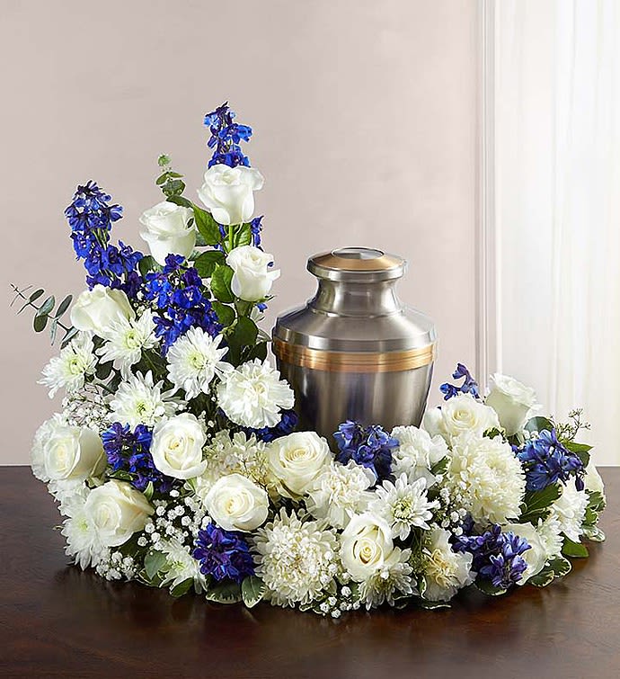 CREMATION WREATH - BLUE AND WHITE - Honor a life so beautifully lived. Our florists artistically hand-design an asymmetrical blue and white table wreath arrangement with roses, carnations, delphinium and more. An urn or framed photograph can be placed in the open center, creating a comforting tribute for the cremation or memorial service. Our florists hand-design each arrangement, so colors and varieties may vary due to local availability Asymmetrical arrangement of blue delphinium and white roses, carnations, cushion poms and football mums; accented with spiral and seeded eucalyptus, gypsophila and variegated pittosporum Send to the cremation service or memorial service; urn or framed photograph can be placed in the center Large arrangement measures approximately 18"H x 18"L Small arrangement measures approximately 17"H x 14"L