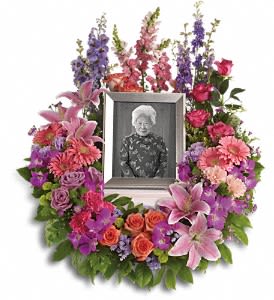 In Memoriam Wreath - Devotion is expressed and beautiful memories cherished with this deep-hued and softly elegant wreath. A lovely reminder of your affection and respect. A mix of dramatic flowers such as purple orchids and asters, orange, dark pink and lavender roses, pink and peach carnations, lavender larkspur, green chrysanthemums, and a range of pink blooms including oriental lilies, gerberas, snapdragons and more. Please note: Arrangement does not include picture frame. Approximately 26" W x 31" H
