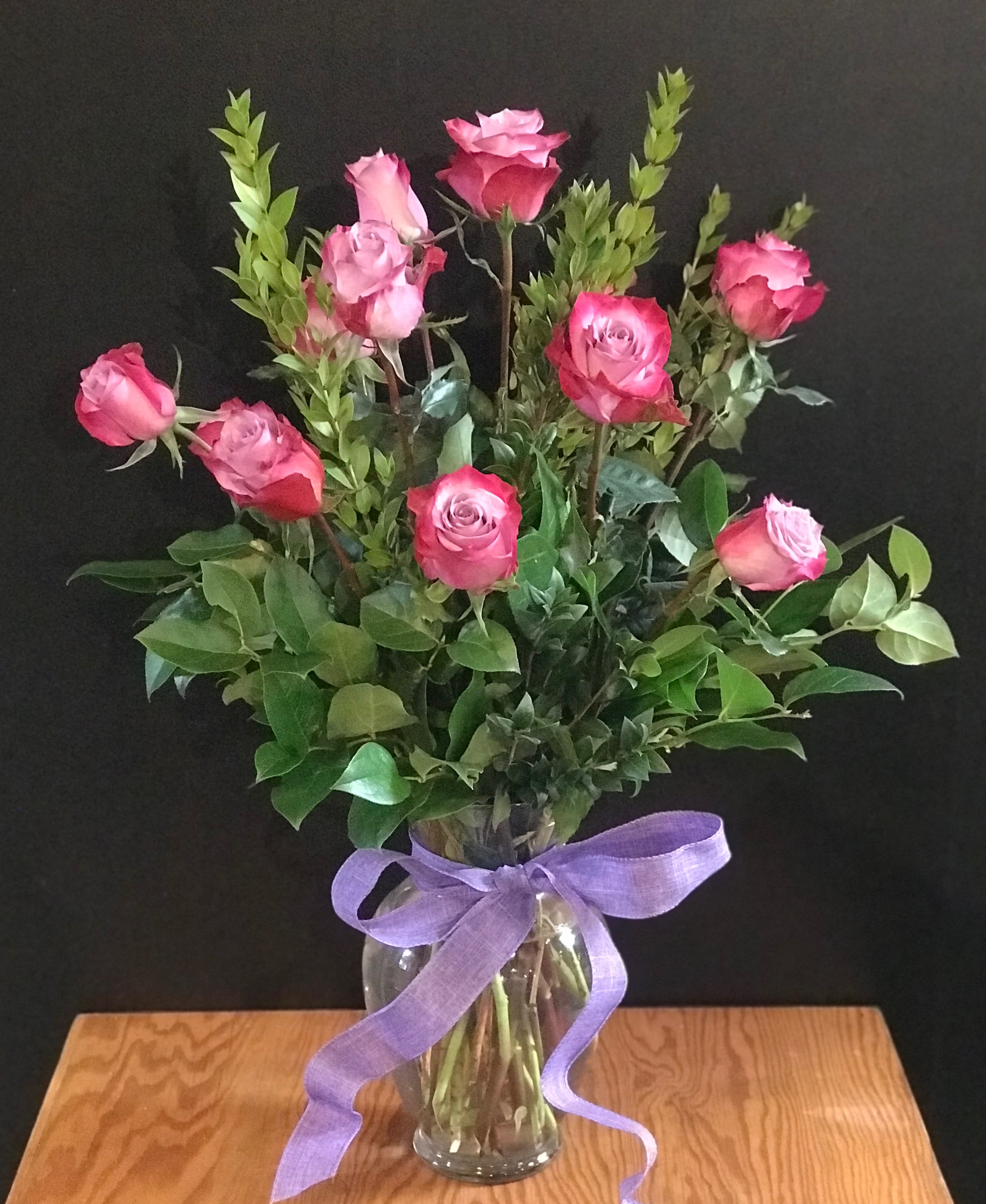 Long stem Purple/lavender Roses  -  These roses are just Berry-licious !  And are the perfect  thoughtful choice  for the purple-lover in your life.   A dozen roses with premium mix greens are arranged in a classic urn vase and finished with a matching ribbon. All our roses are open cut roses, which means they are on the plant longer. This allows them to be a stronger cut flower and have a longer vase life. 