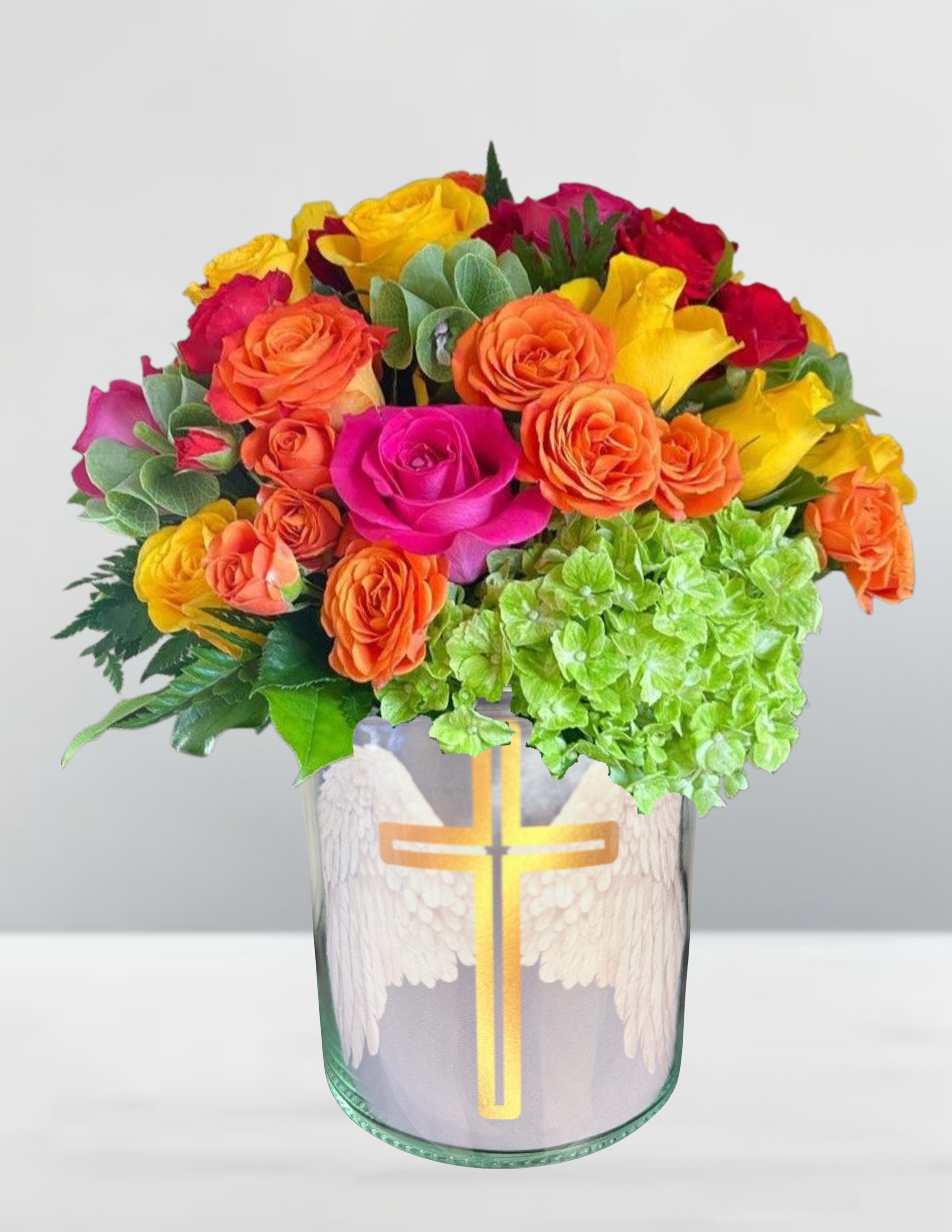 Wings of light  - Wings of Light A radiant symphony of color and grace, this arrangement lifts the spirit like a prayer on the wind. Blushing roses in shades of sunset—amber, coral, and petal-pink—nestle beside luminous green hydrangeas, their softness echoing the hush of reverence. Wisps of greenery weave through the bouquet like whispered blessings, while the golden cross and angel wings adorning the vase serve as a quiet testament to hope, remembrance, and divine presence. Perfect for moments of reflection, celebration, or heartfelt tribute, Wings of Light is more than a floral display—it’s a gentle embrace from above.