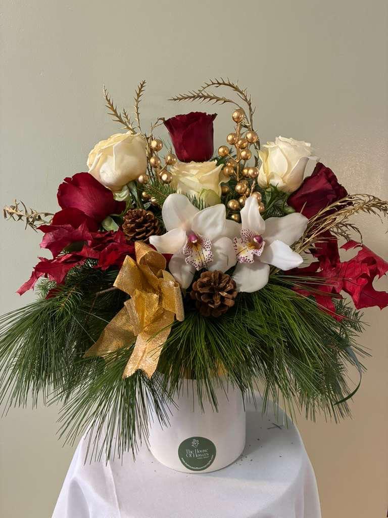 Crimson Noel by The House of Flowers - This Christmas arrangement features a generous selection of premium red and white roses, beautifully paired with elegant white orchids. Designed in a large, substantial base, it is richly accented with fresh pine greenery, pine needles, pinecones, and refined golden holiday details.  Handcrafted with care and intention, this arrangement offers abundant volume, rich textures, and a timeless seasonal look. Perfect as a statement centerpiece, holiday décor, or a meaningful Christmas gift.  Each piece is created in limited quantities to ensure freshness, quality, and exclusivity. 