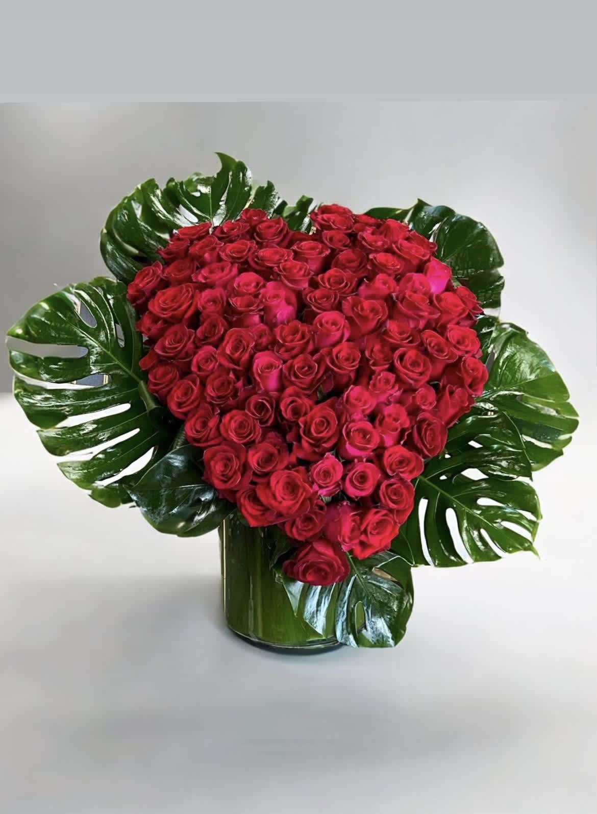 A New Day - This vase arrangement is overflowing with red Roses in the shape of a heart, surrounded by Monstera leaves