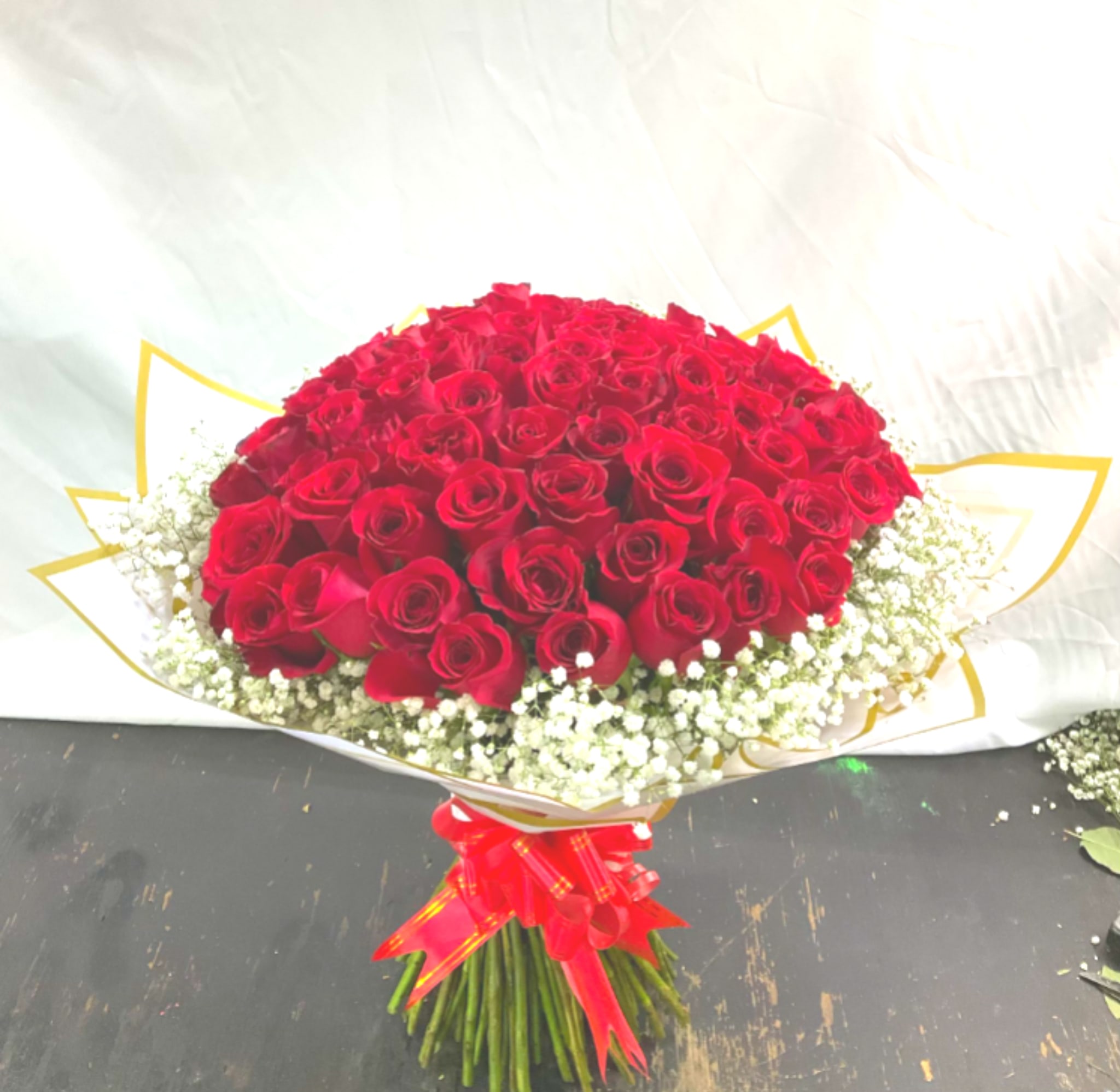 100 Reasons Why - Make a grand romantic gesture with 100 Reasons Why — an opulent bouquet of 100 premium long stem red roses, elegantly wrapped and framed by delicate baby’s breath. Each rose is a symbol of passion, love, and deep devotion. Finished with a luxurious red ribbon, this show-stopping arrangement is perfect for anniversaries, proposals, or celebrating someone truly unforgettable.