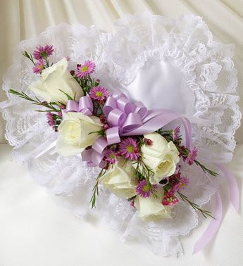 Lavender and White Satin Heart Casket Pillow - Express the love in your heart with this touching tribute.  This satin casket pillow – in the shape of a heart – is adorned with a spray of white roses, lavender Monte Casino, purple waxflowers and a satin ribbon This particular style of tribute is often sent by children or grandchildren and delivered directly to the funeral home. Our florists use only the freshest flowers available so varieties and colors may vary. Measures approximately 9”L x 9”W