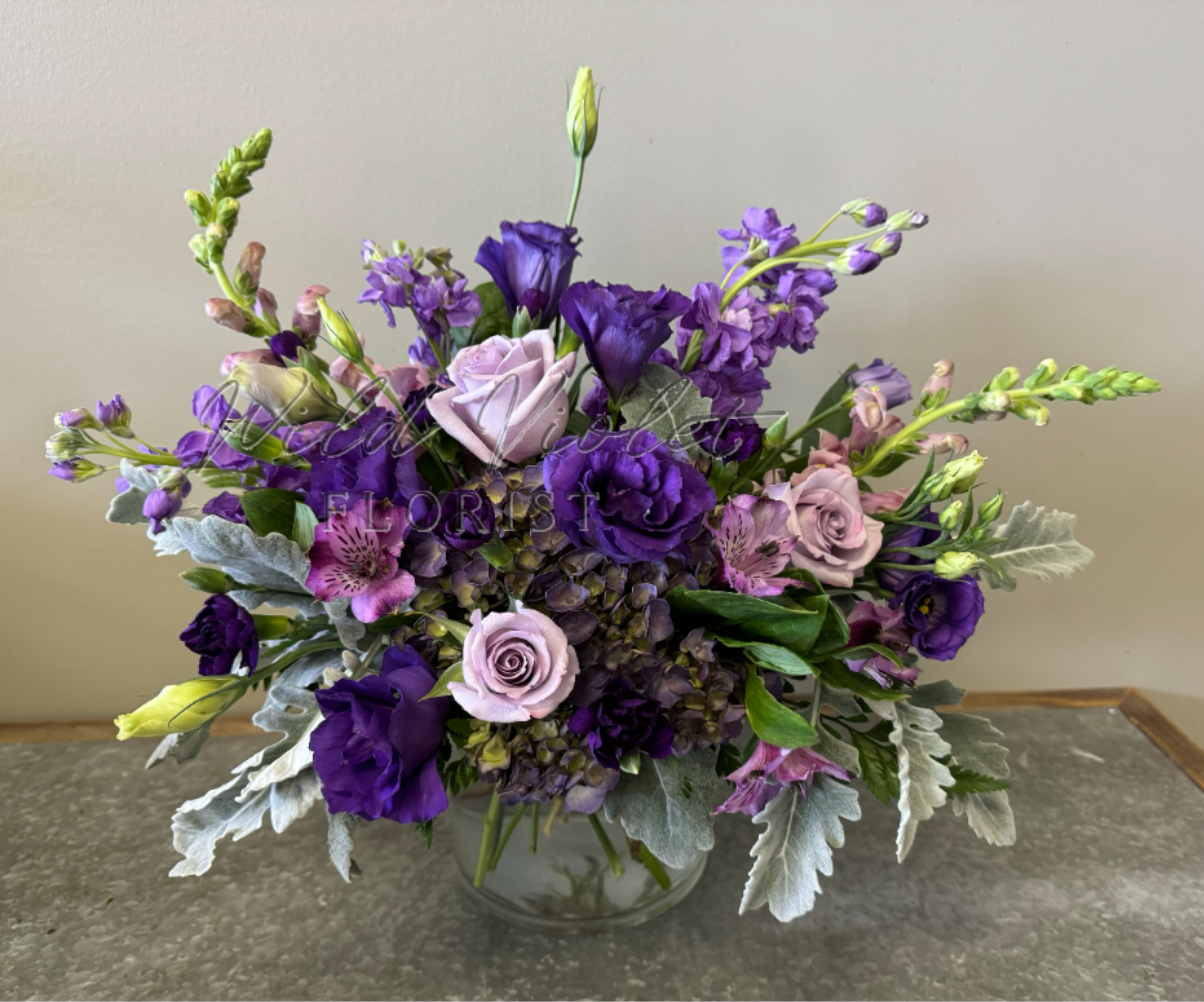 February Amethyst Bouquet - Birthstone Collection What better way to celebrate your loved one's birthday than with our February Amethyst  Bouquet! Hand-designed with a stunning gathering of light and deep purple blooms, lush greenery and silver touches, it’s a thoughtful sentiment filled with the gorgeous beauty of an amethyst stone.  ATTENTION! If you are ordering this arrangement on a different month other than what it's respected month is, there will be substitutions for certain flowers depending on seasonal availability. We will stay within the same color scheme and design style!  PLEASE NOTE: Florist reserves the right to make modifications to the design based on seasonality and accessibility of blooms and vases. Any modifications made will honor the palette, intent, and feeling of the pictured design. Contact floral designer directly with any specifications or concerns.