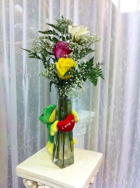 Purity, Passion, Friendship - This whimsical arrangement comes with Roses, Babys Breath and seasonal greenery with Keepsake Green/Yellow Frog w/Love You Red Heart in a clear glass vase. 