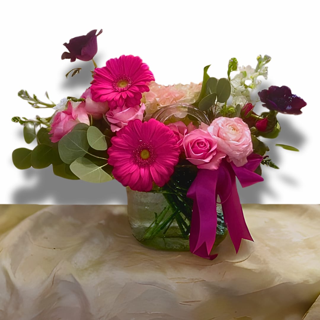  Limited Edition Glass Purse VAL2507 - Limited Edition Glass Purse VAL2507 This elegant bouquet, bursting with pink gerbera daisies, soft roses, and lush greenery, radiates the warmth of Love and affection. The vibrant magenta ribbon tied around the vase adds a festive touch, making it a perfect gift for Valentine's Day, a heartfelt gesture on Mother's Day, or any occasion where expressing love is the centerpiece. It's a floral celebration of tenderness, beauty, and meaningful connection.