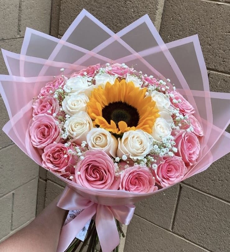 Sunflower Rosy Delight Bouquet - A gorgeous round bouquet that highlights a stunning sunflower at the center surrounded by pink and ivory roses. Wrapped in soft pink cellophane with a satin bow, this bouquet is sweet, modern, and full of charm — perfect for birthdays or “thinking of you” moments.