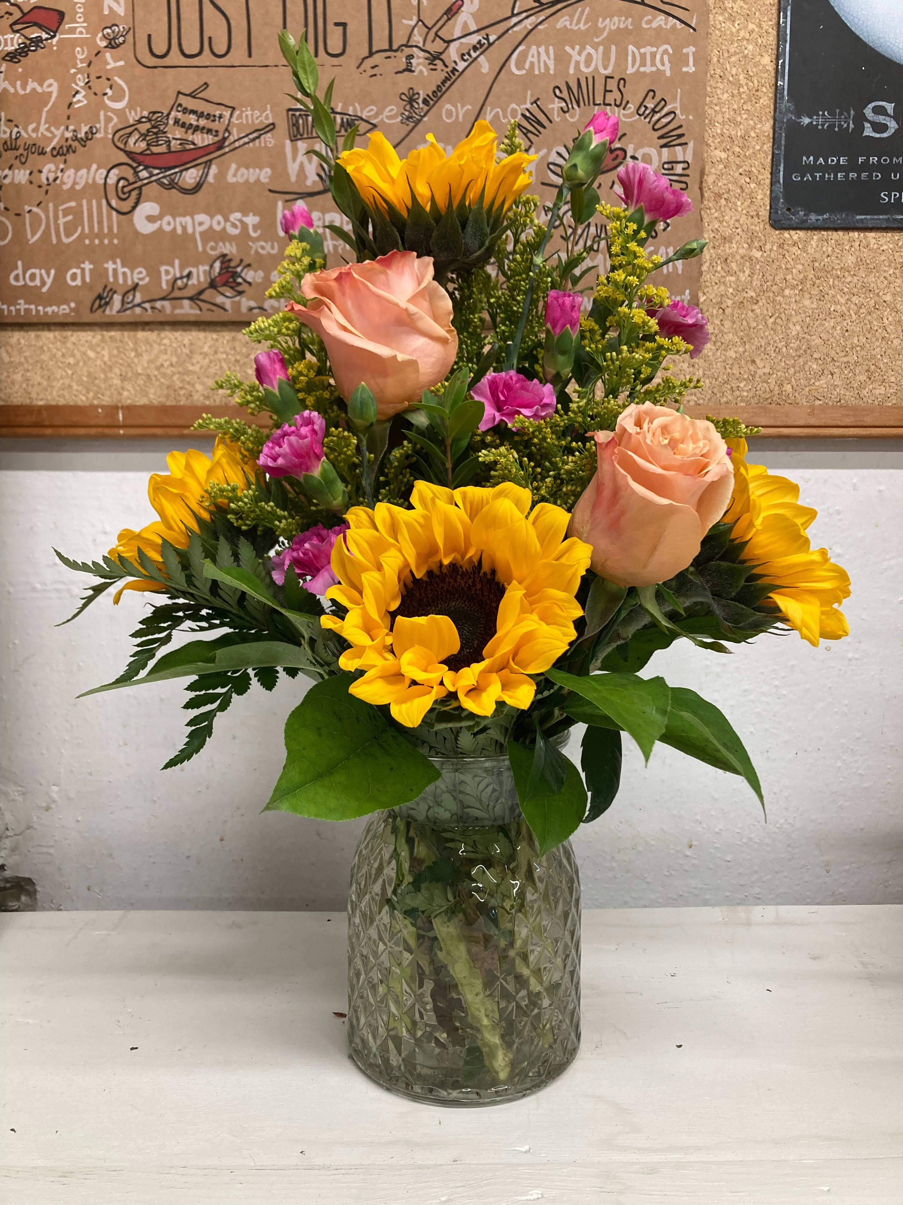 Sunny in Trinidad - It’s sunny here almost every day, this arrangement is sunny too. A mix of Sunflowers and roses and other blooms in a clear glass vase. Bright, cheerful sunflowers  will make someone’s day a lot brighter.