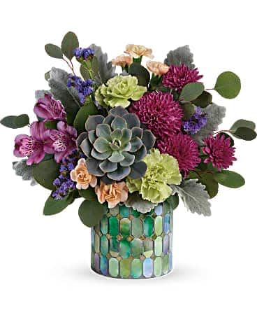 Teleflora's Marvelous Mosaic Bouquet - When only marvelous will do! Make a stylish statement with this unique bouquet of jewel toned blooms and succulents, artfully arranged in a stained glass inspired mosaic glass cylinder. Purple alstroemeria, green carnations, peach miniature carnations, purple cushion spray chrysanthemums, and purple sinuata statice are arranged with silver dollar eucalyptus, dusty miller, and a large green echeveria succulent. Delivered in a Marvelous Mosaic cylinder.