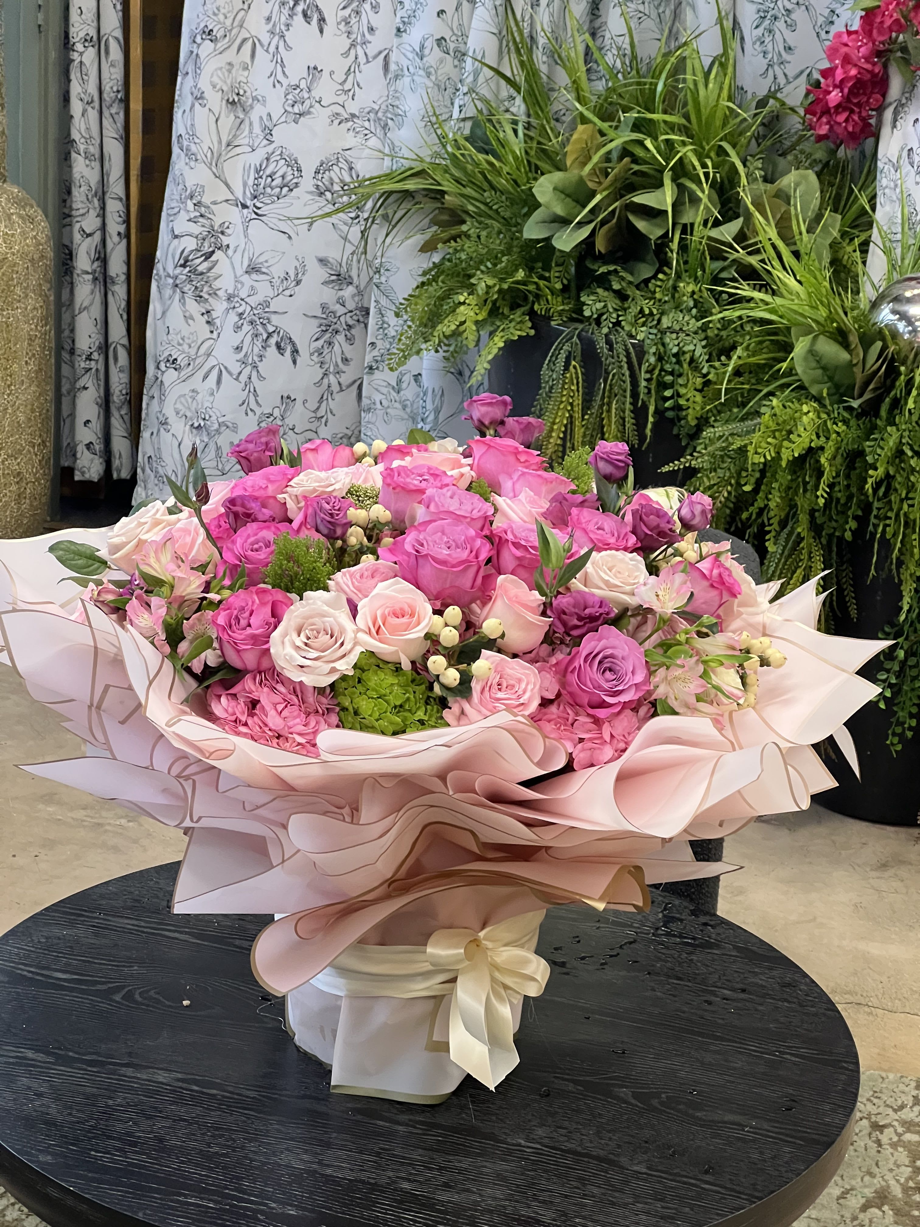 Jewel - This gorgeous floral arrangement features shades of pink Roses with Hypericum and other select blooms, in a stylishly wrapped glass vase