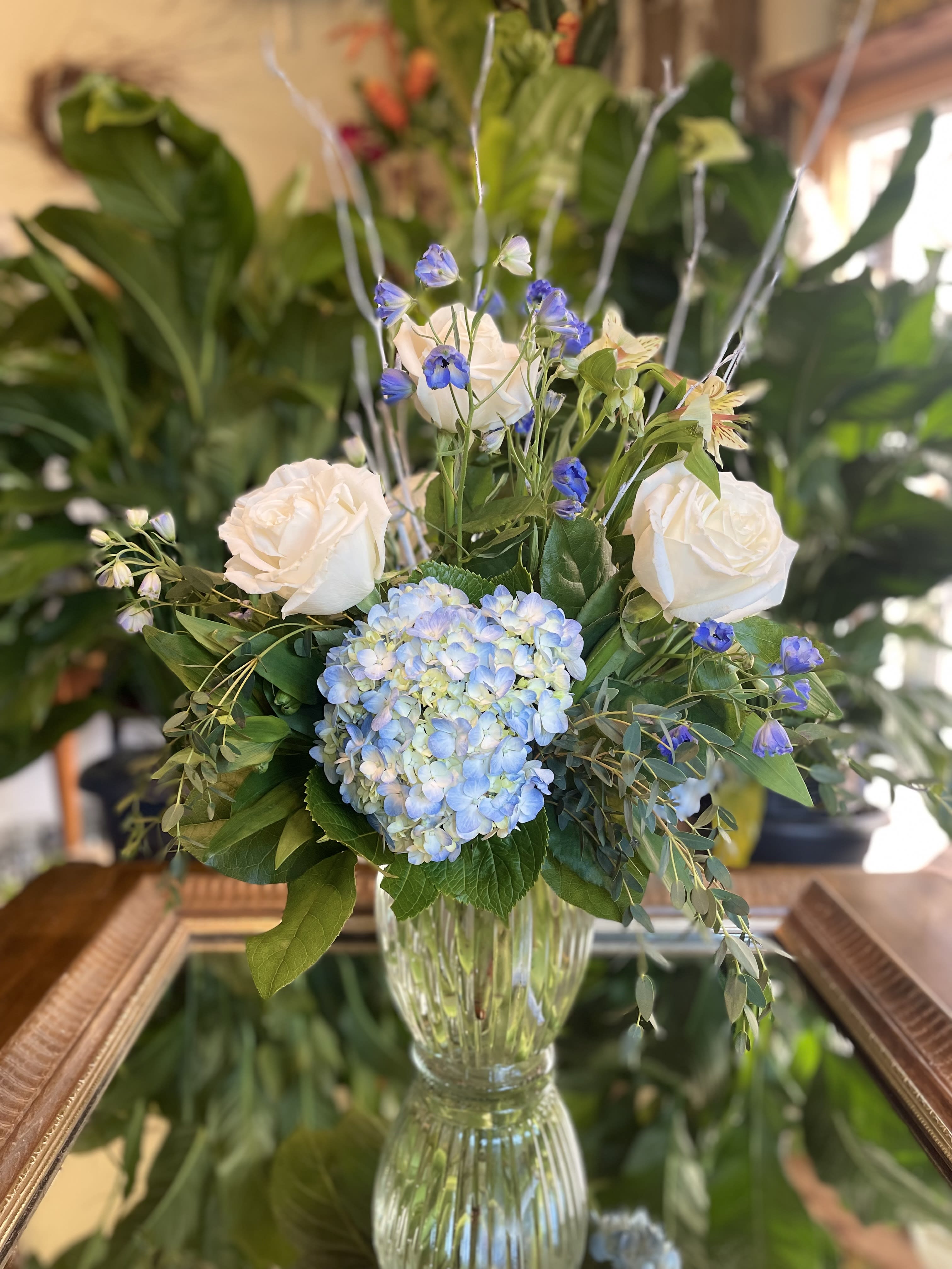 January Special  - A blushing blue winter arrangement with delphiniums, white roses, and blue hydrangeas. Accented with white branches to tie together this frosty theme. 