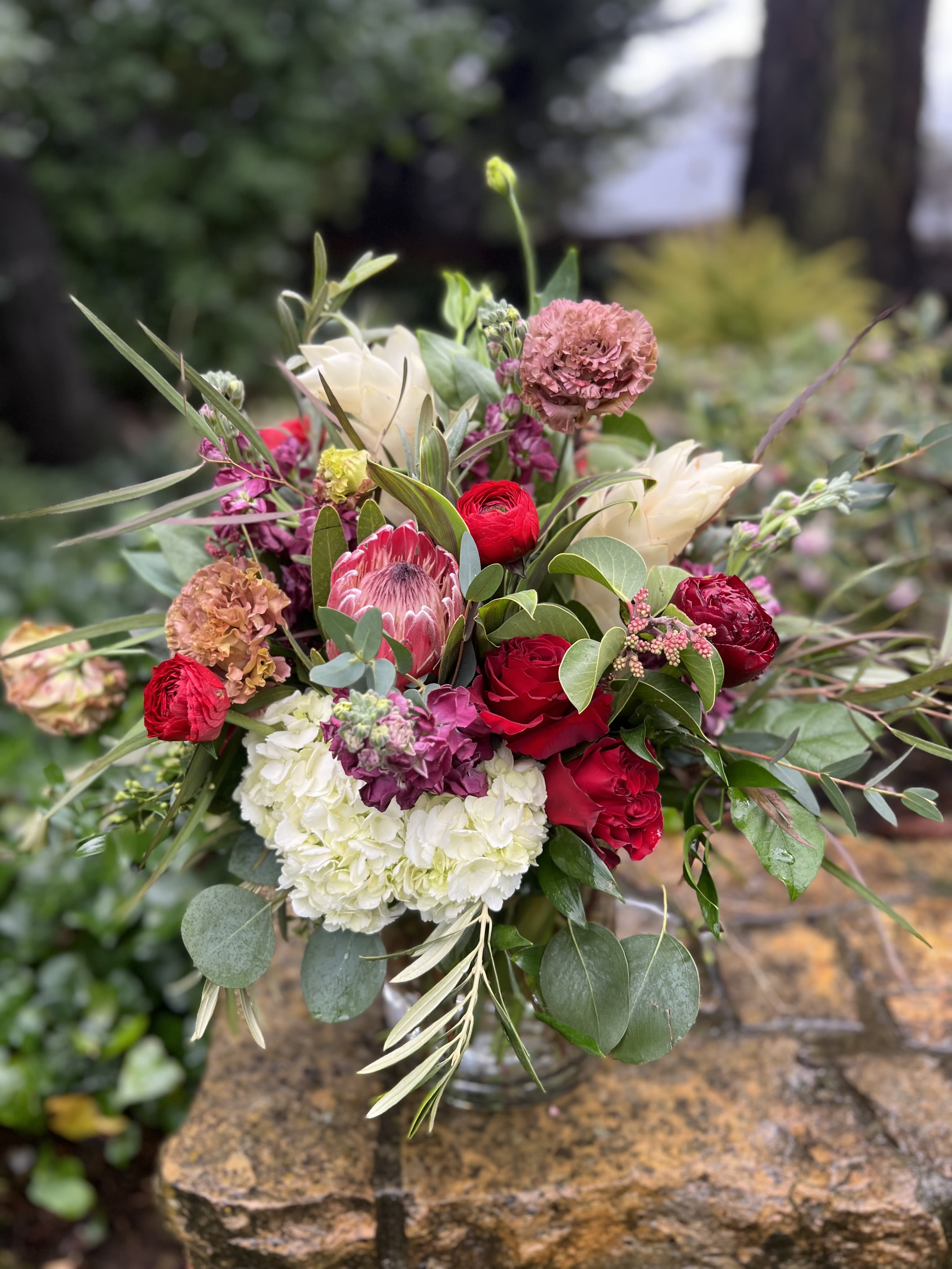 Loves Tropicals  - A romantic island get away she certainly is! Reds and tropicals become one with this collection of protea and ginger accented with roses, peonies and ranunculus. 
