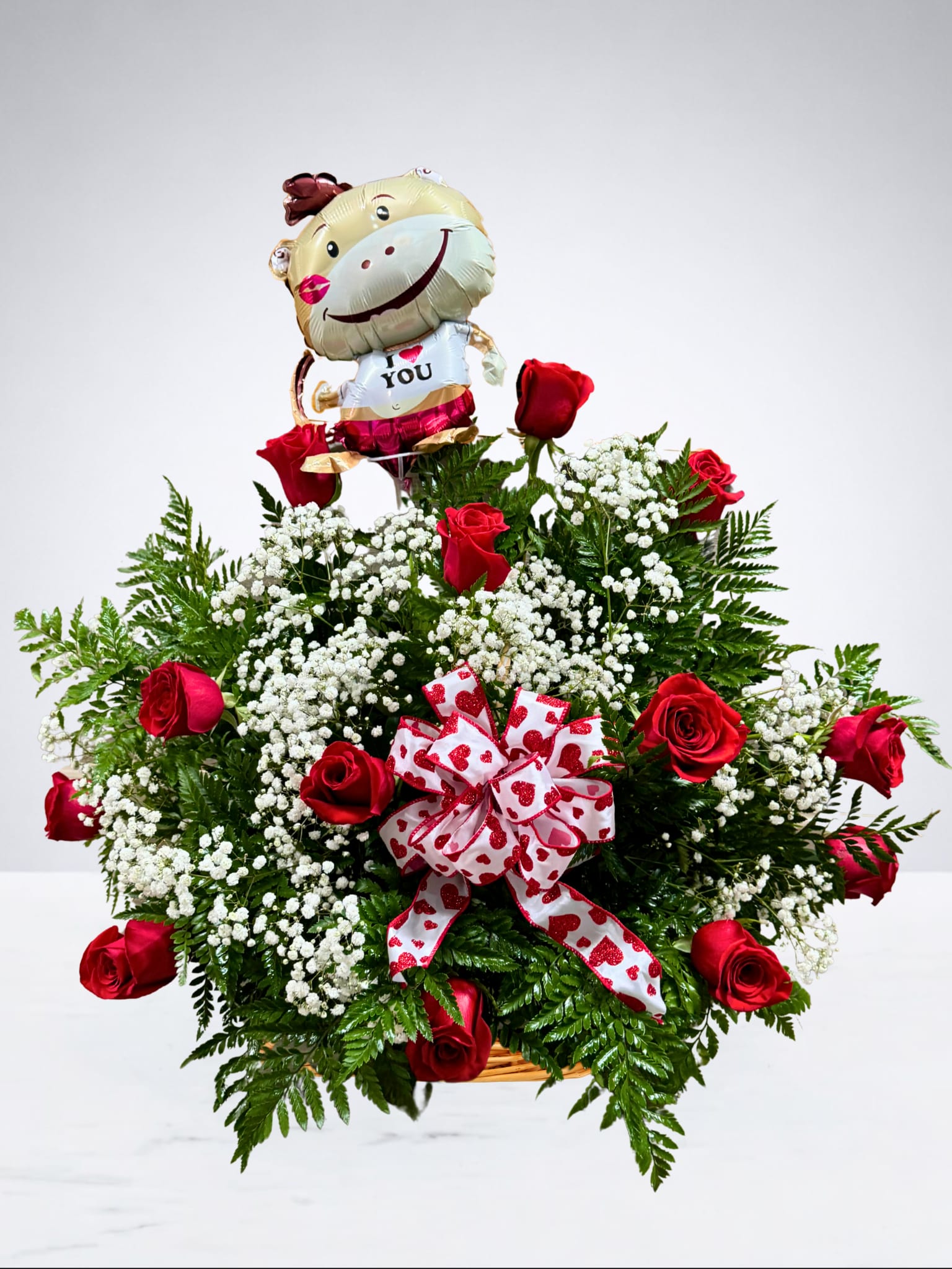 Rose-Mantic Basket  - Nothing says "I love you" like a classic basket of red roses and airy baby's breath. Perfectly tied together with a signature heart ribbon and a cheerful balloon to brighten their day.  Please note: The themed balloon included will vary based on availability