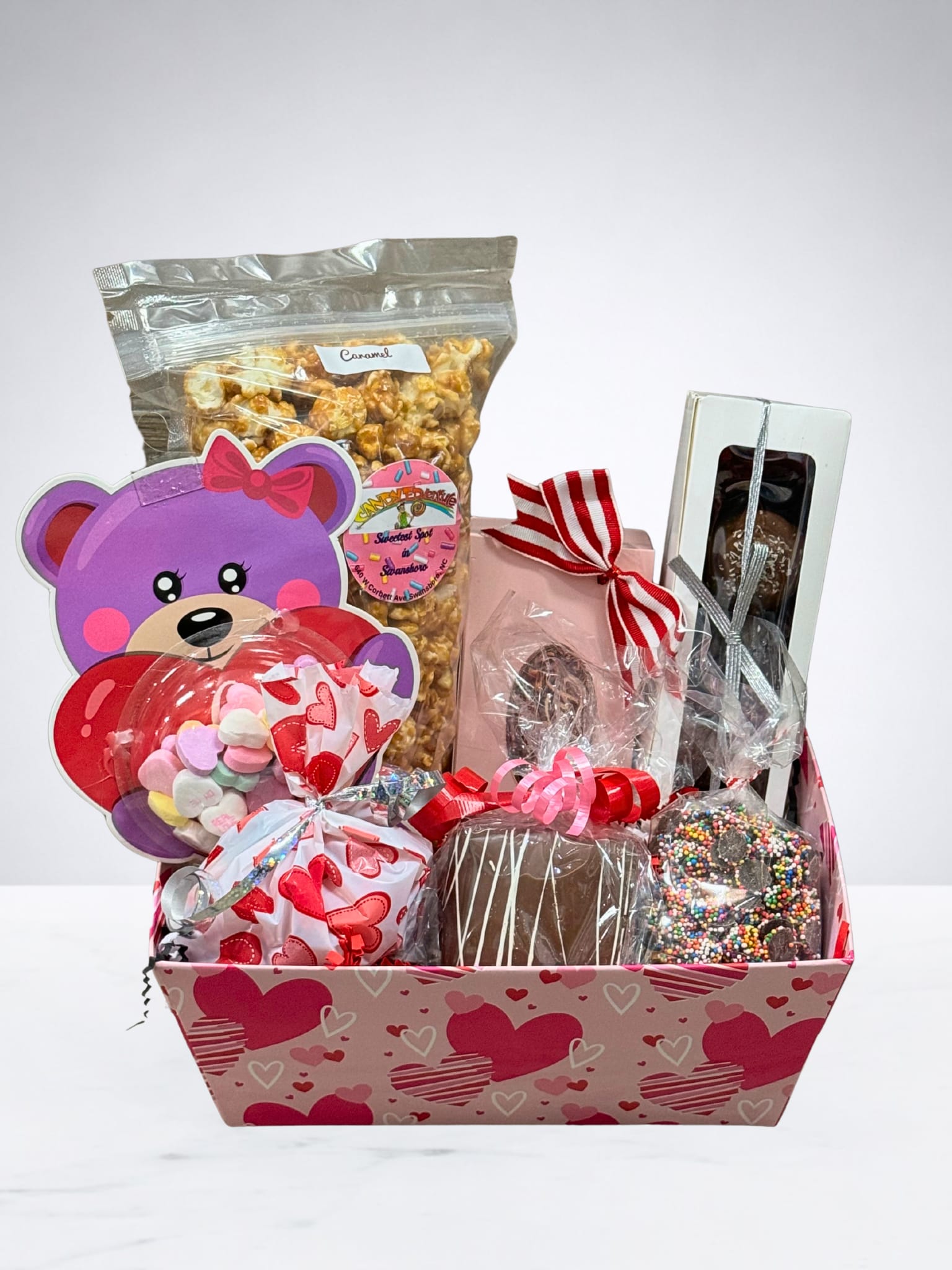Sweetheart Stash - Overflowing with love and sugar, this adorable Valentine’s Day goodie basket is packed with festive treats that are sure to make hearts smile! From chocolatey delights to colorful, candy-filled surprises, every piece is wrapped with care and sprinkled with Valentine charm. Perfect for gifting to a sweetheart, friend, child, or anyone who deserves a little extra love this season. Sweet, playful, and irresistibly fun—this basket is a Valentine’s Day treat they won’t forget!   Included in the basket: -Caramel Popcorn -1/4 Pound Chocolate Walnut Fudge -1/4 Pound Chocolate Peanut Butter Fudge -Assorted Truffles -Chocolate Covered Graham Crackers -Chocolate Nonpariels -Conversational Heart Card -Liquor Chocolates (For Adults Only)