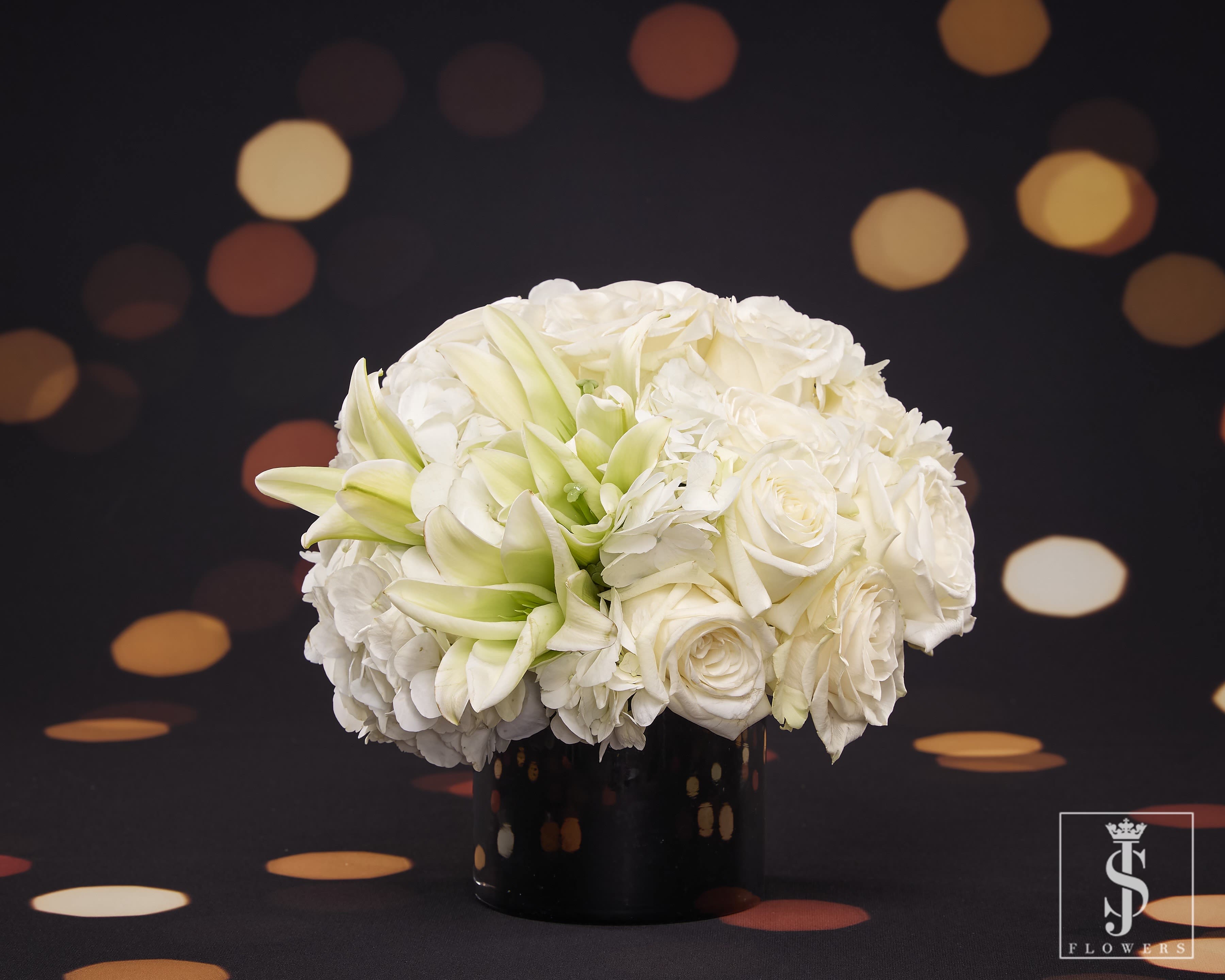 A Reflection - Ring in the New Year with this stunning arrangement that exudes elegance and sophistication. A graceful blend of white roses, symbolizing purity and fresh beginnings, and white lilies, representing renewal and celebration, this design is a perfect fit for welcoming new opportunities. Paired with lush white hydrangeas for fullness and texture, the arrangement radiates modern luxury and timeless charm. Arranged in a sleek black vase, it’s the ideal centerpiece to elevate your New Year's festivities, creating an atmosphere of serenity and style as you celebrate the year ahead.